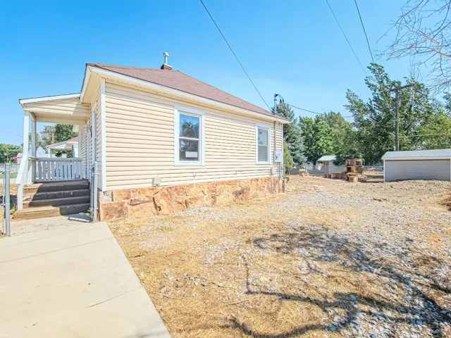 Exterior featuring horizontal siding, a covered porch with white railings, a concrete walkway, and a detached shed