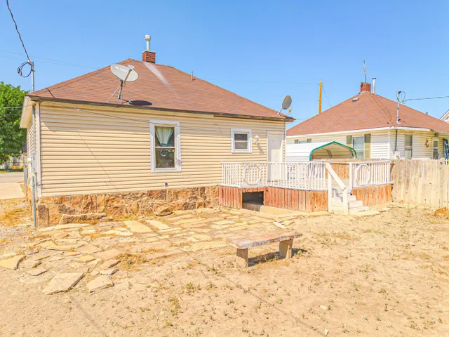 Rear exterior featuring a wood deck with white railing, stone foundation, and a partial flagstone patio