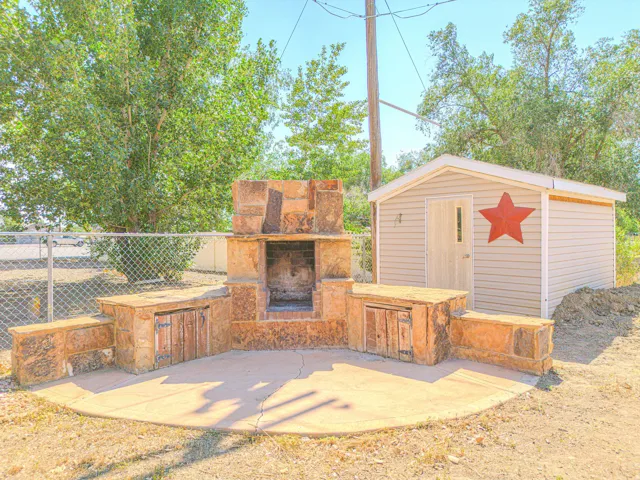 Outdoor stone fireplace with built-in storage, circular concrete patio, and a storage shed with siding