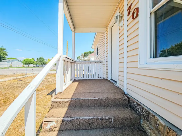 Front porch featuring a white railing, steps with textured surfacing, and light-colored siding