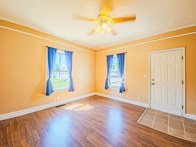Wood-finish flooring with a tile entryway, two windows, and a ceiling fan with integrated lighting