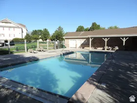 Rectangular swimming pool with a concrete surround, enclosed by fencing, featuring a nearby covered patio area