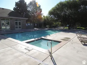 Outdoor pool featuring a built-in spa, concrete decking, and a brick-clad building