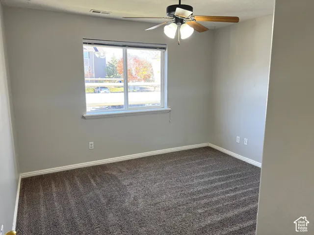 Light gray painted walls, brown patterned carpet, a single window, and a ceiling fan with integrated lighting