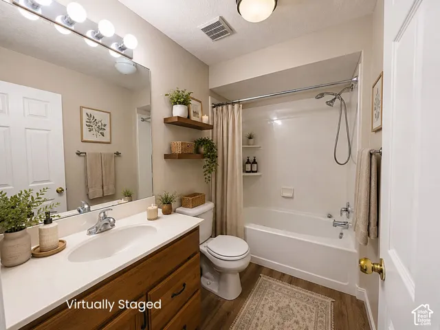 Bathroom featuring a wood-finish vanity with a single basin sink, full-width mirror, and a shower-over-tub combination with a wall-mounted showerhead
