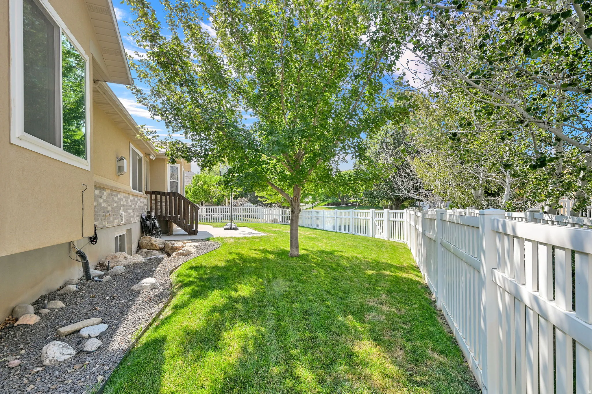 Manicured lawn with a white privacy fence, mature trees, and a gravel-lined rock bed
