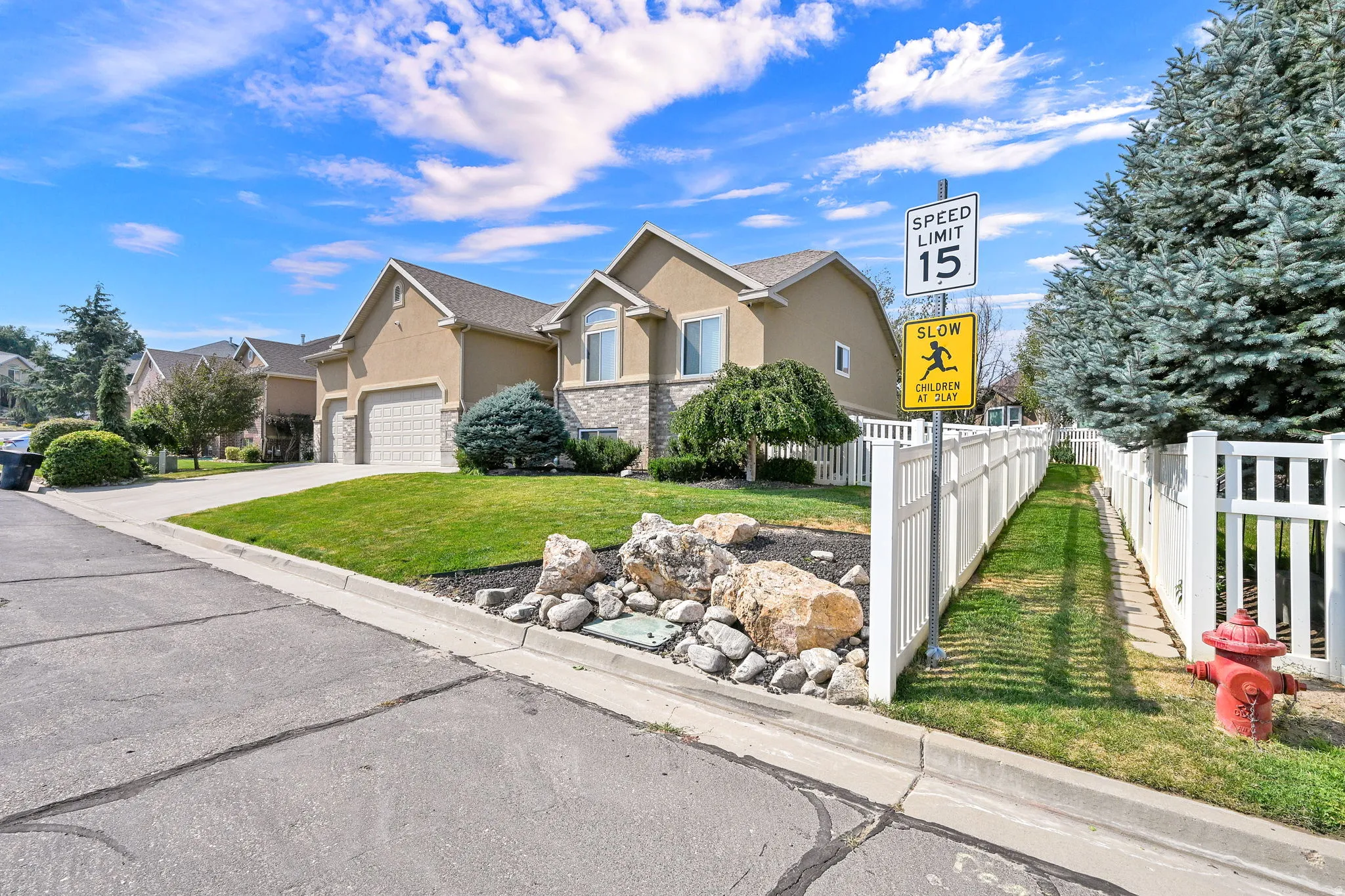 Stucco and stone exterior with a two-car garage, manicured lawn, and mature landscaping