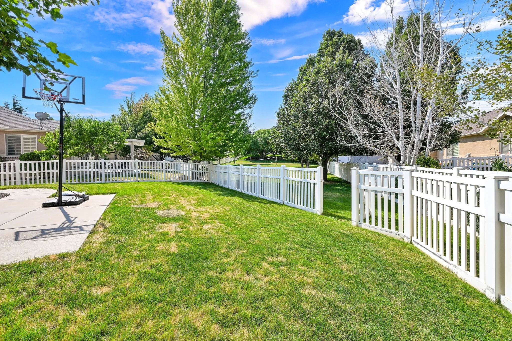 Expansive lawn area featuring a white picket fence, mature trees, and a concrete patio
