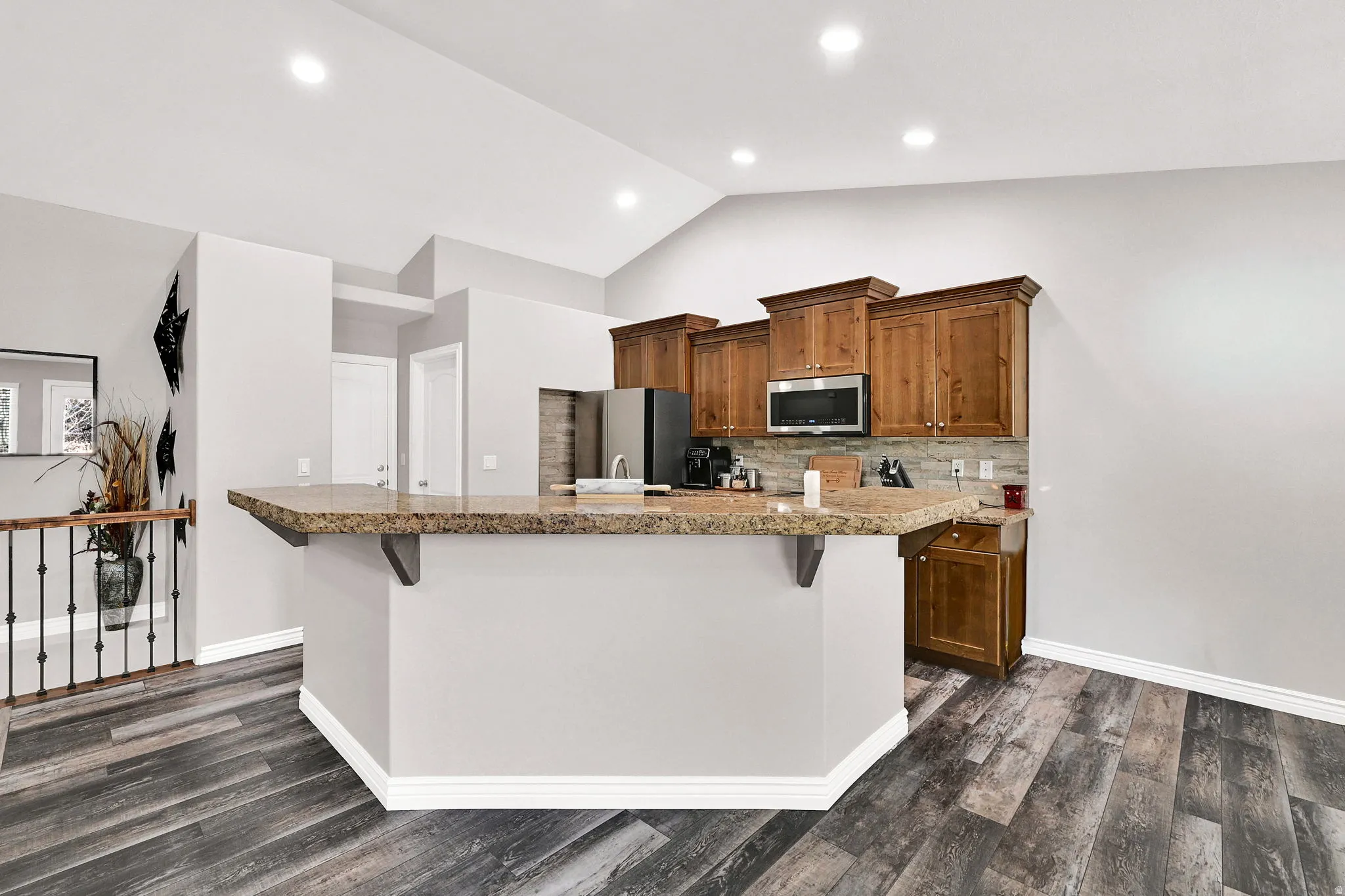 Wood-finish flooring, vaulted ceiling, recessed lighting, wood cabinetry, and a stone-look countertop