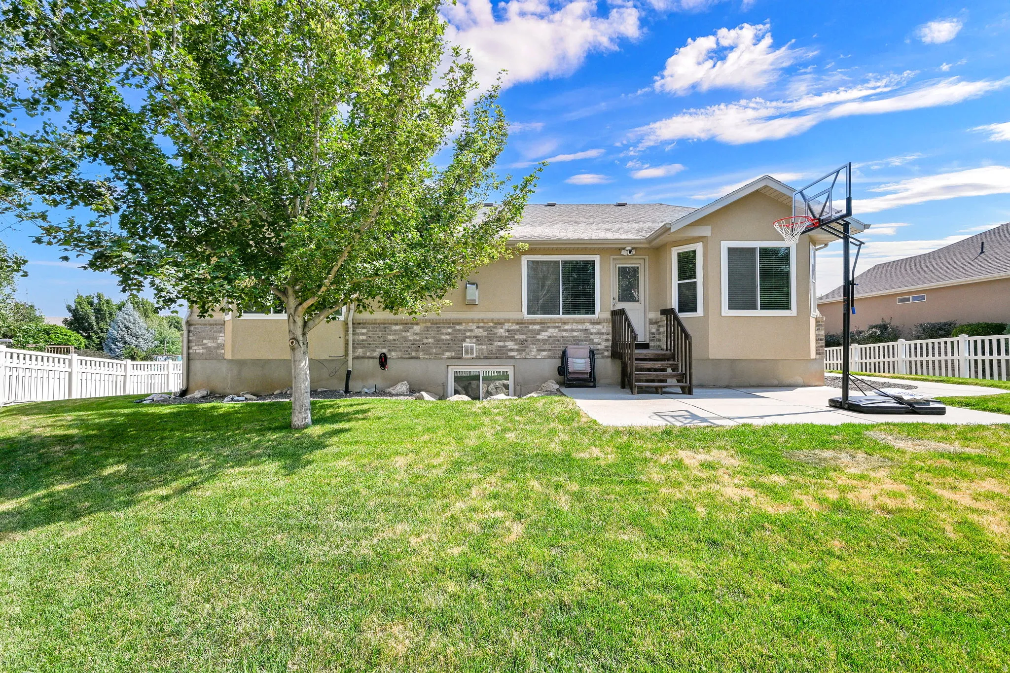 Rear exterior with a concrete patio, wood stairs, multiple windows, and a white picket fence