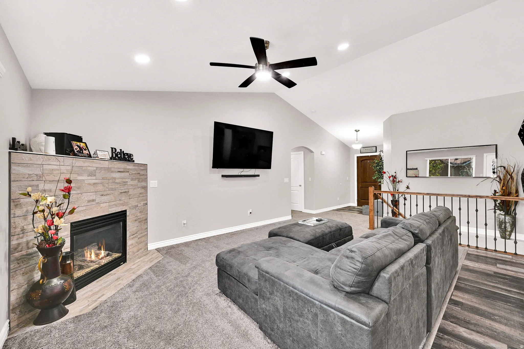 Vaulted ceiling, recessed lighting, ceiling fan, stone-tiled fireplace, and wood-finish flooring