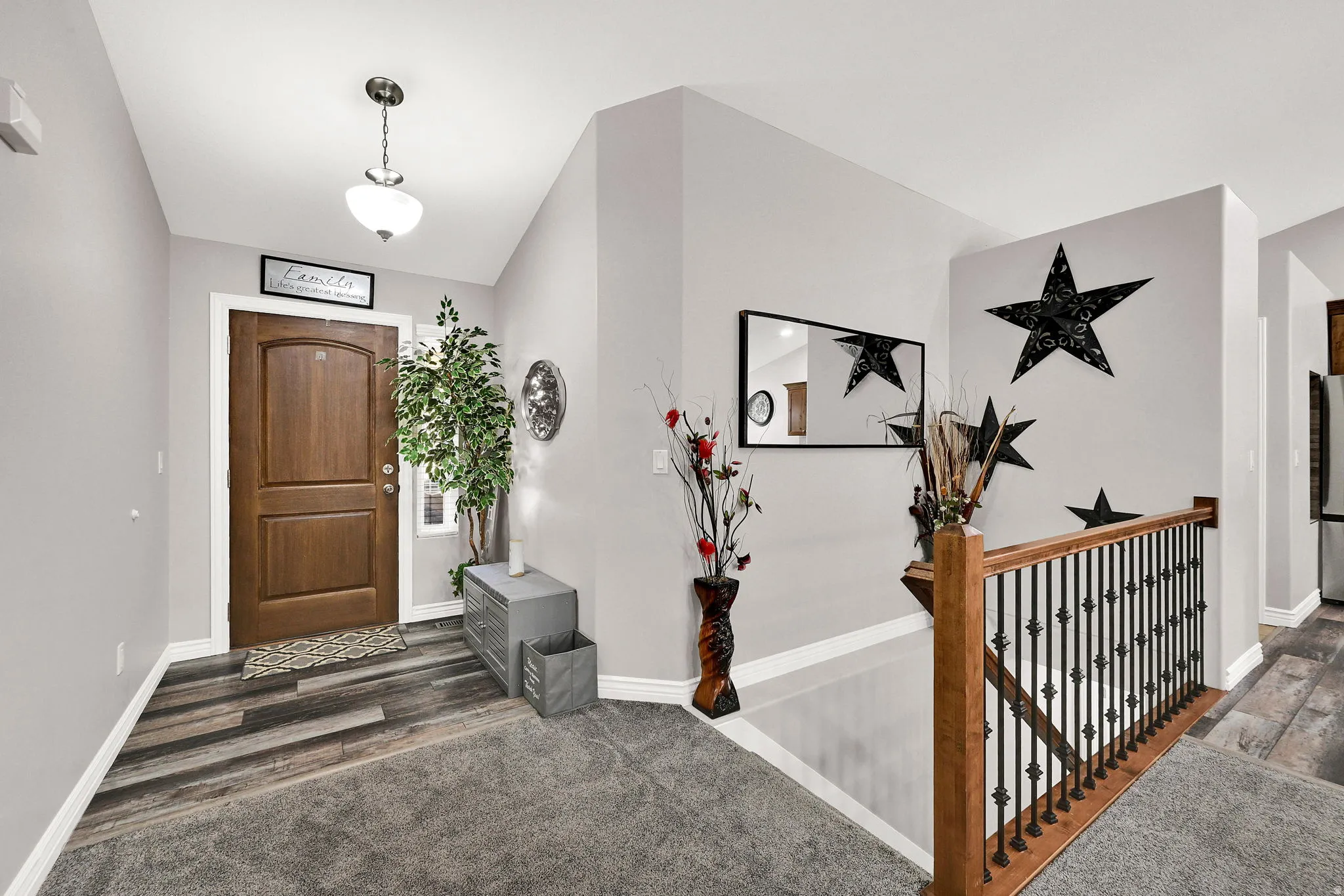 Hardwood entry door with arched panel details, wood-finish flooring, and a decorative pendant light fixture
