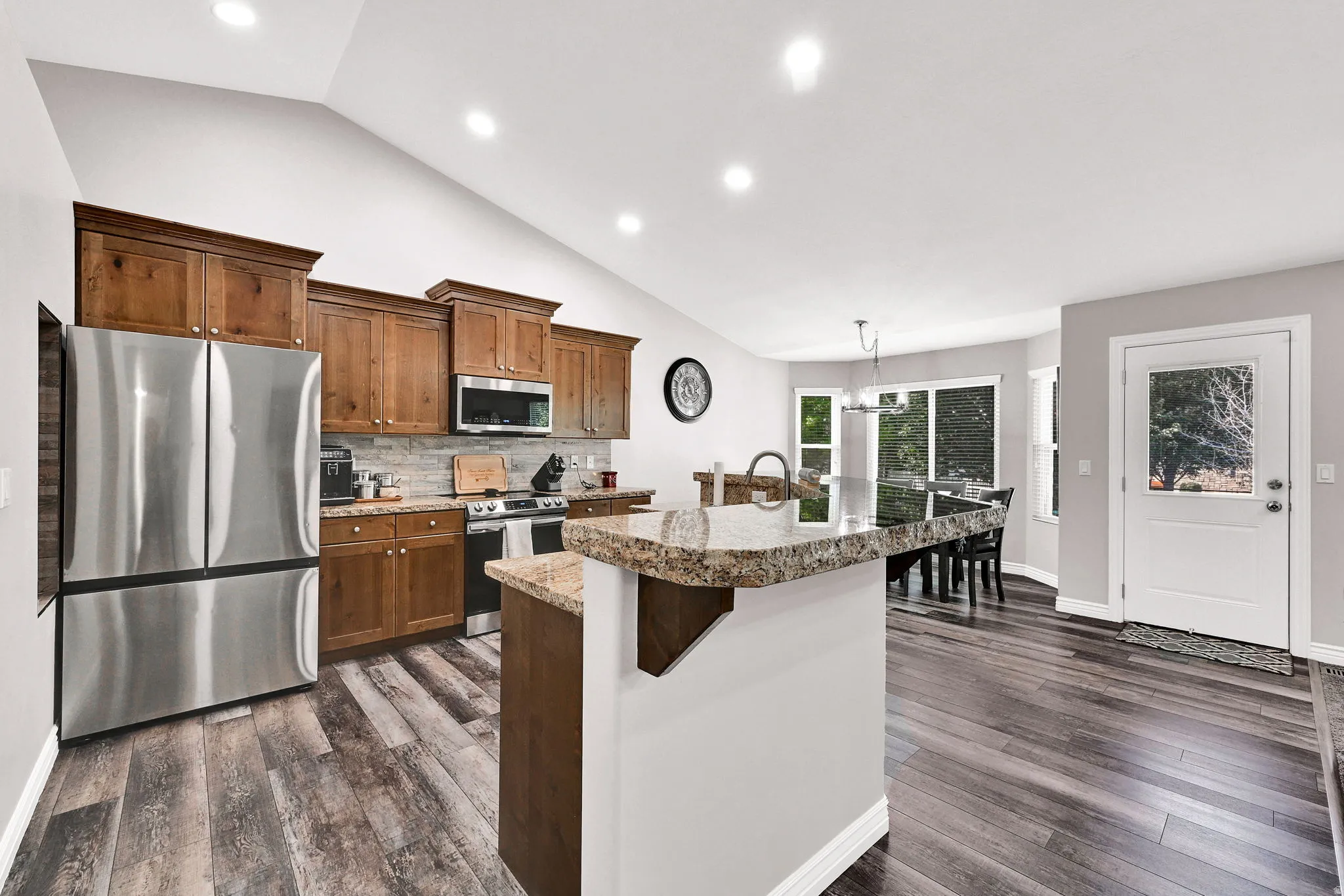Vaulted ceiling, wood-finish flooring, stainless steel appliances, wood cabinetry, and a granite-finish island
