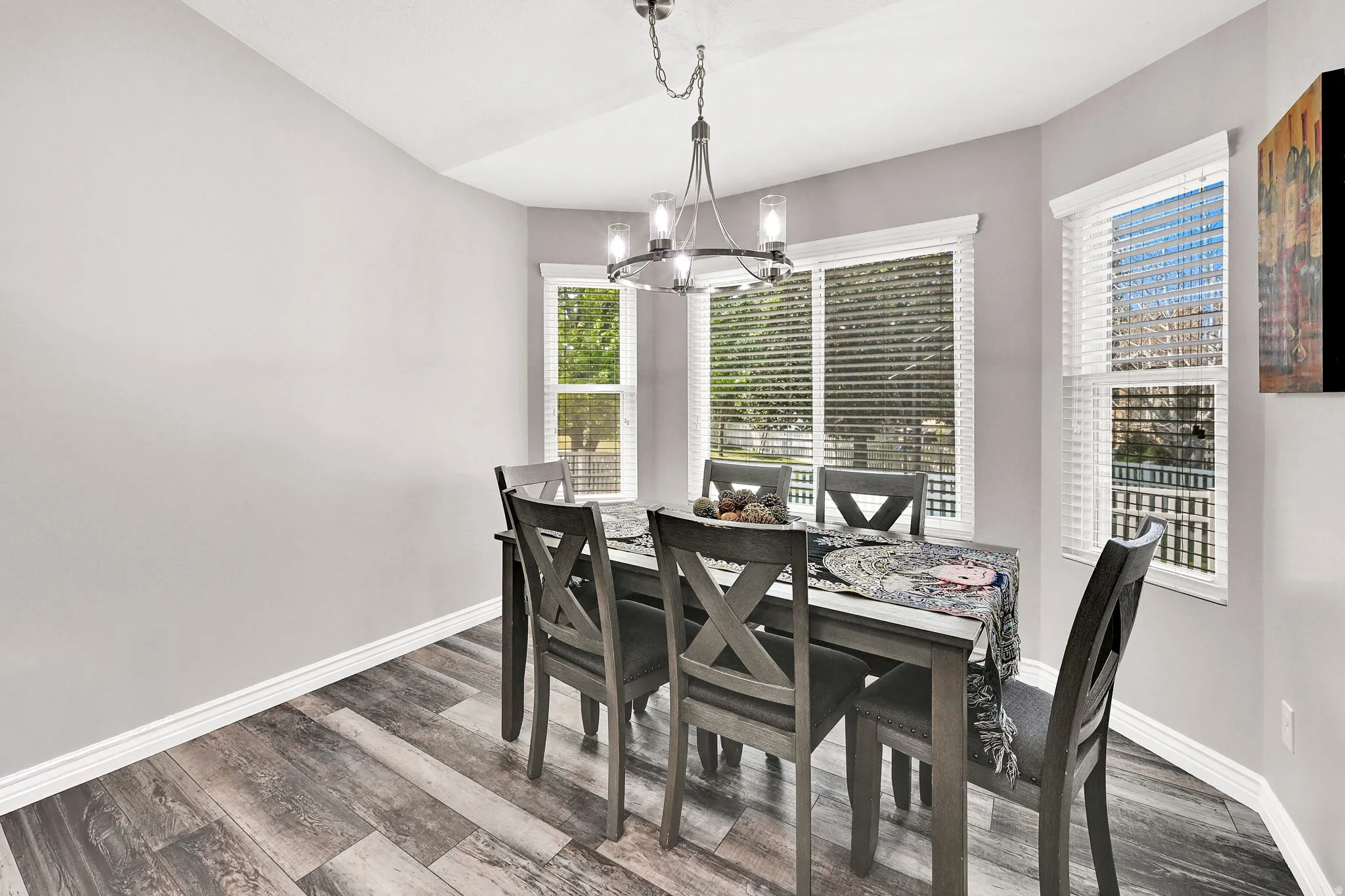 Dining area featuring wood-finish flooring, a contemporary chandelier, and multiple windows with blinds