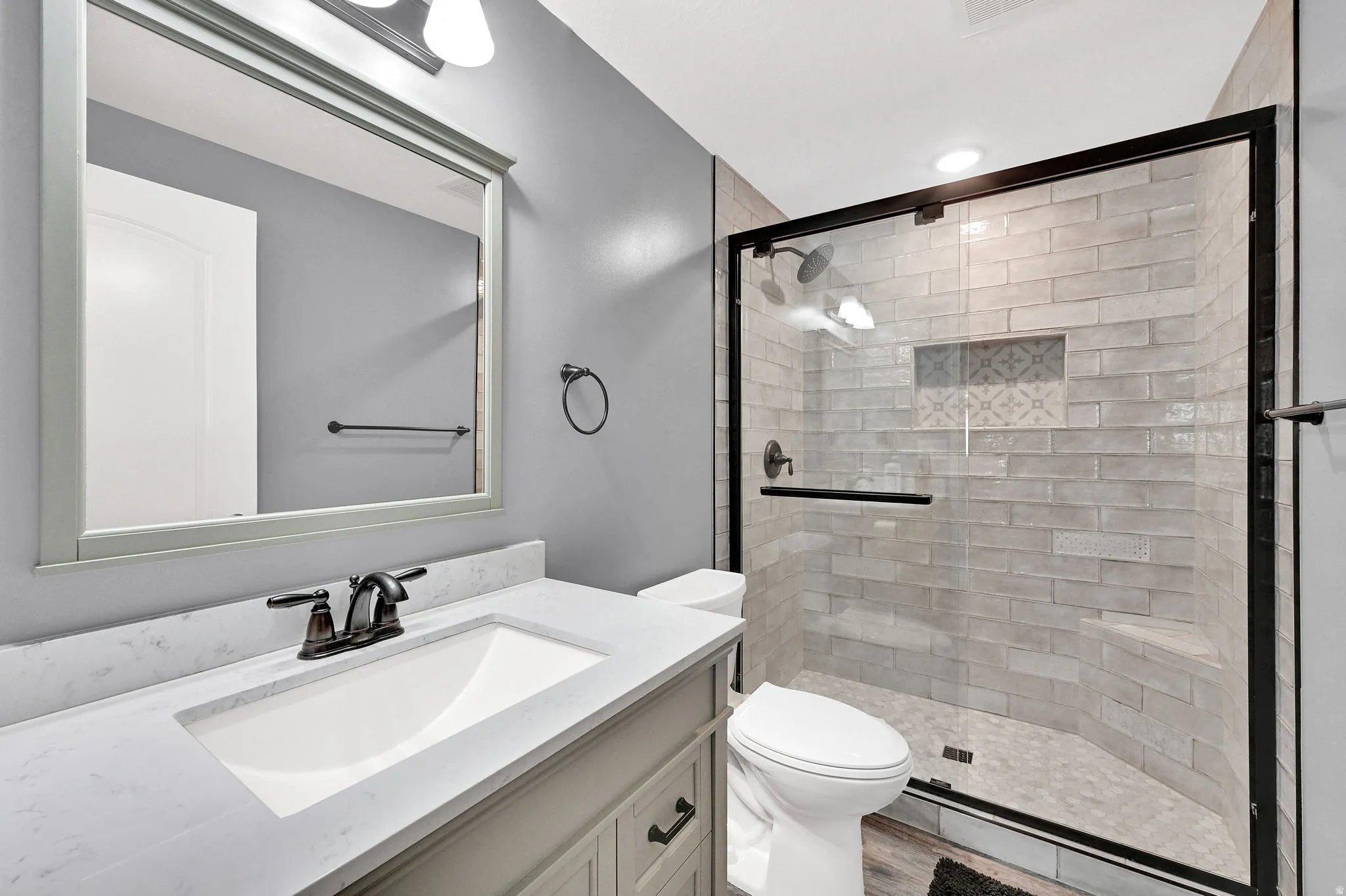 Vanity with an integrated sink and bronze-finish faucet, framed mirror, and enclosed shower with tile surround and built-in bench