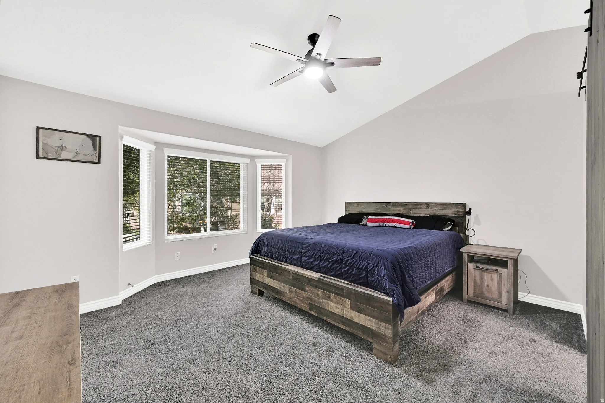 Vaulted ceiling with a ceiling fan, bay windows with blinds, and gray carpeting