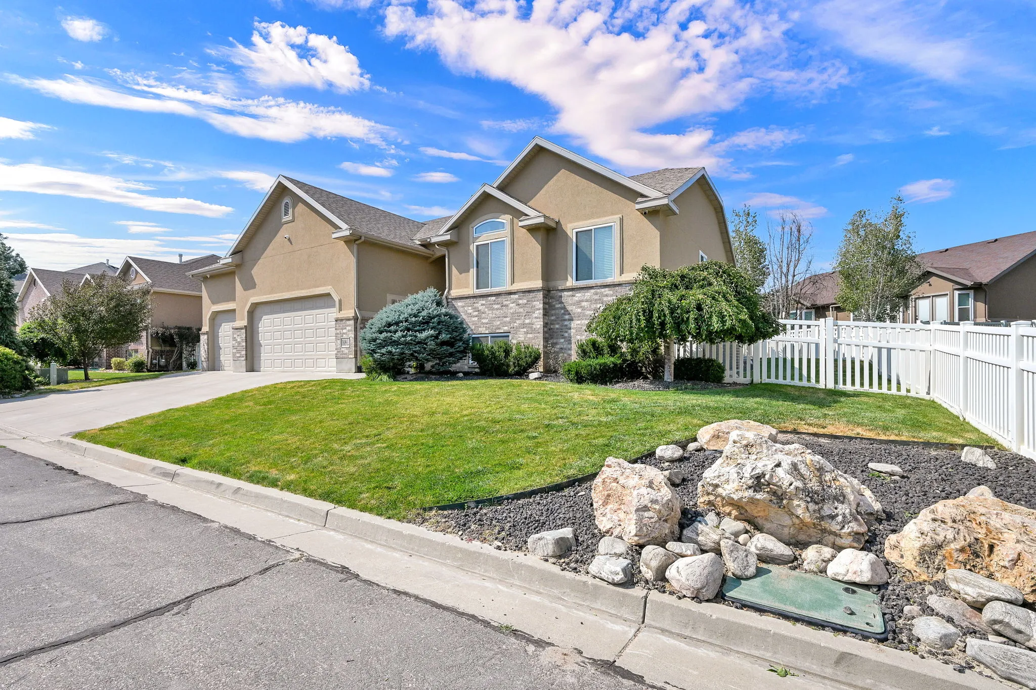 Stucco exterior with stone accent, arched window, attached two-car garage, manicured lawn, and white picket fence
