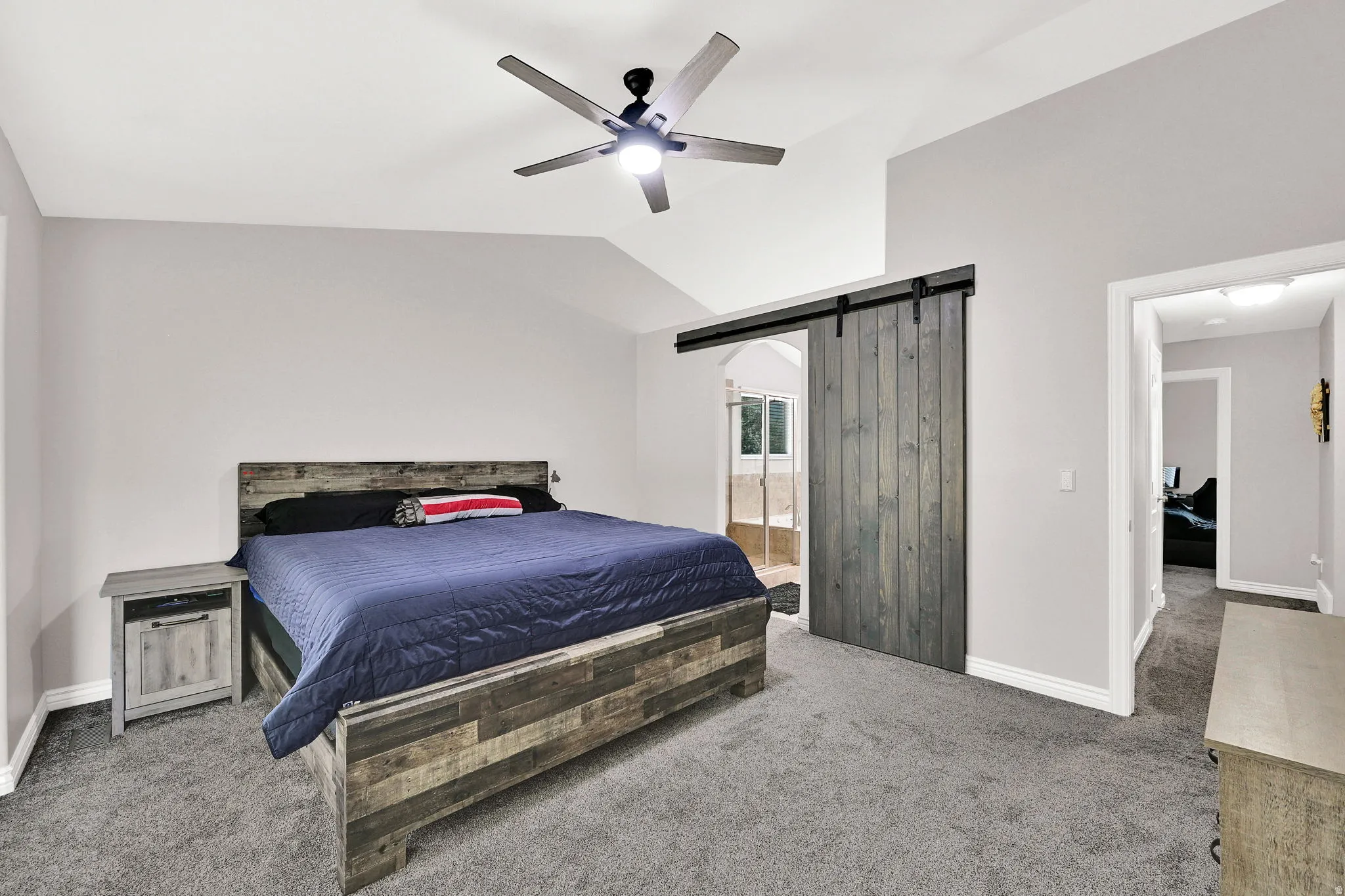 Vaulted ceiling with a ceiling fan, plush carpet flooring, and a barn door entry to an additional space