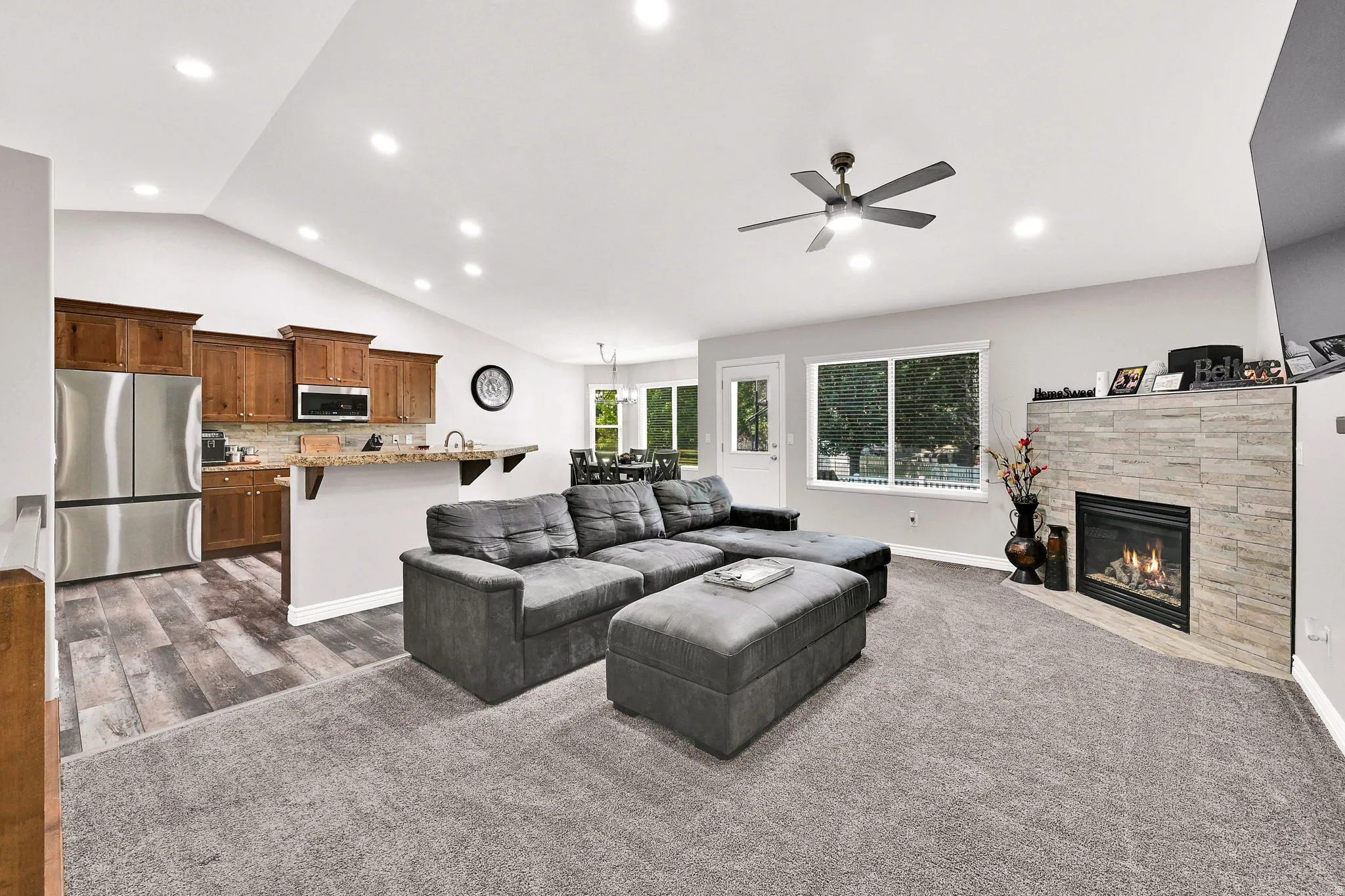 Open concept living area featuring a stone-clad fireplace, vaulted ceiling with recessed lighting, and wood-finish flooring