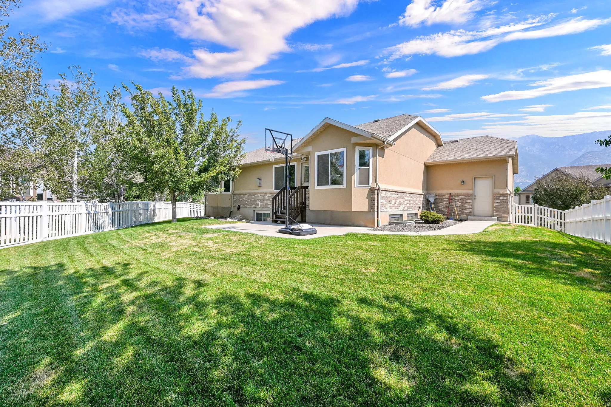 Expansive backyard featuring a manicured lawn, established trees, and a white picket fence