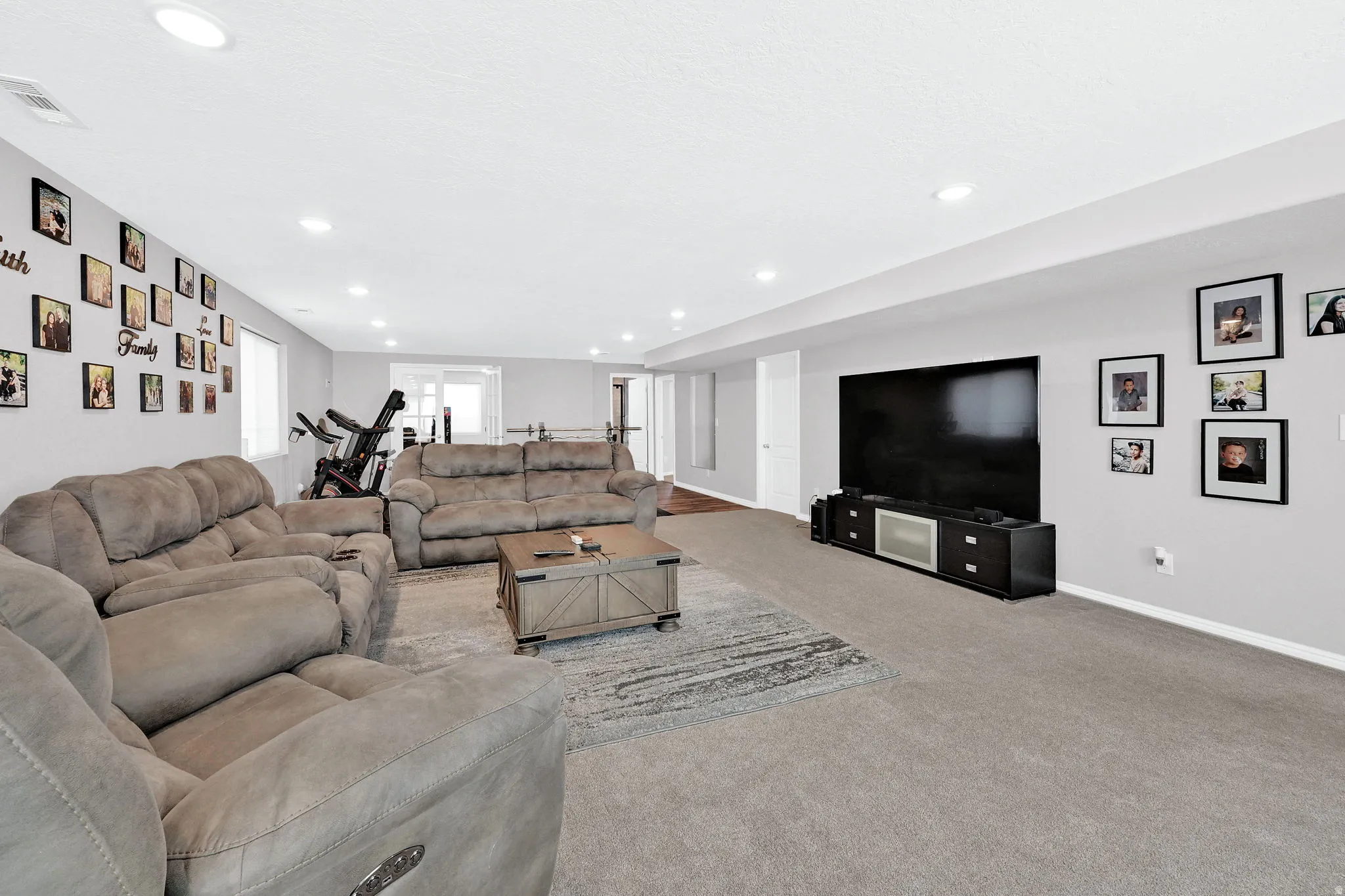 Recessed lighting illuminates a spacious room featuring light gray walls and gray carpeting