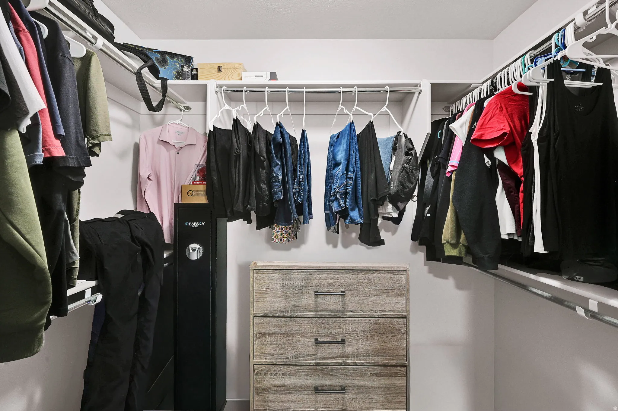 Walk-in closet featuring white wire shelving, multiple hanging rods, and a three-drawer wood-finish dresser with dark hardware
