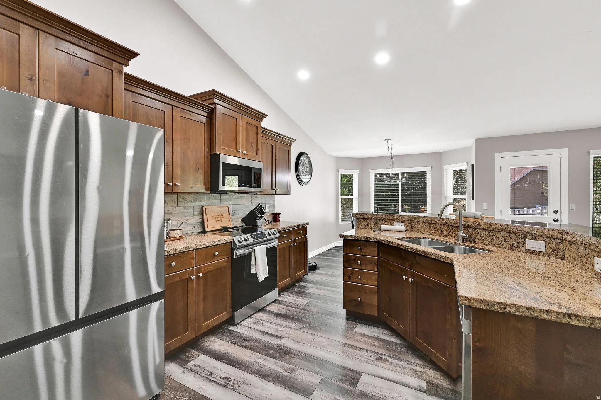 Kitchen featuring warm wood cabinetry, stainless steel appliances, stone countertops, and wood-finish flooring