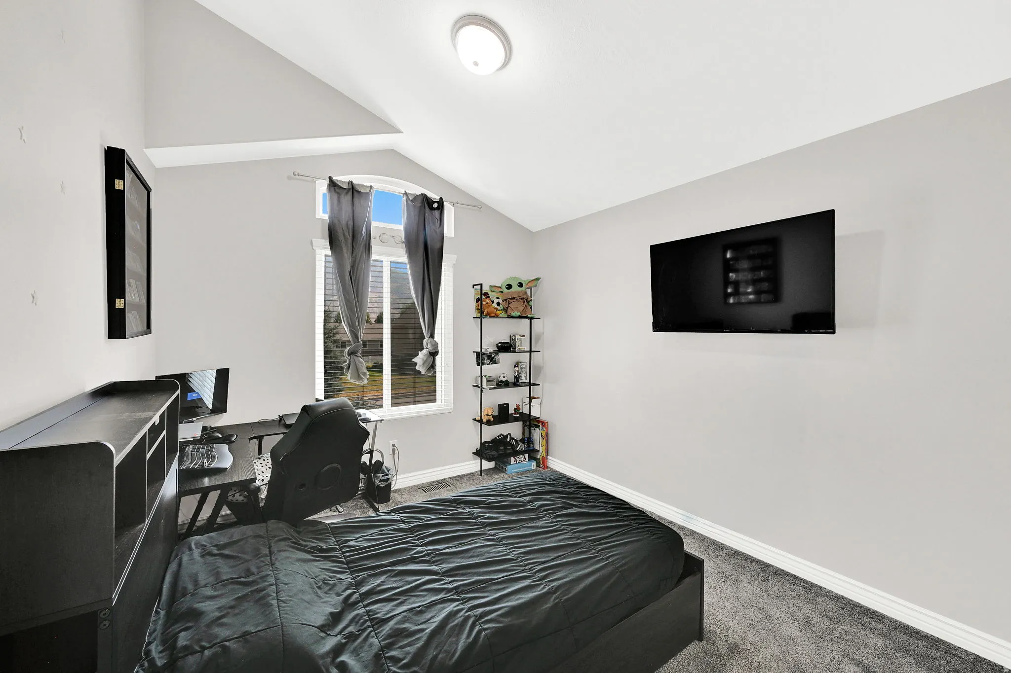 Vaulted ceiling, arched window, wall-mounted light fixture, light gray walls, gray carpeting