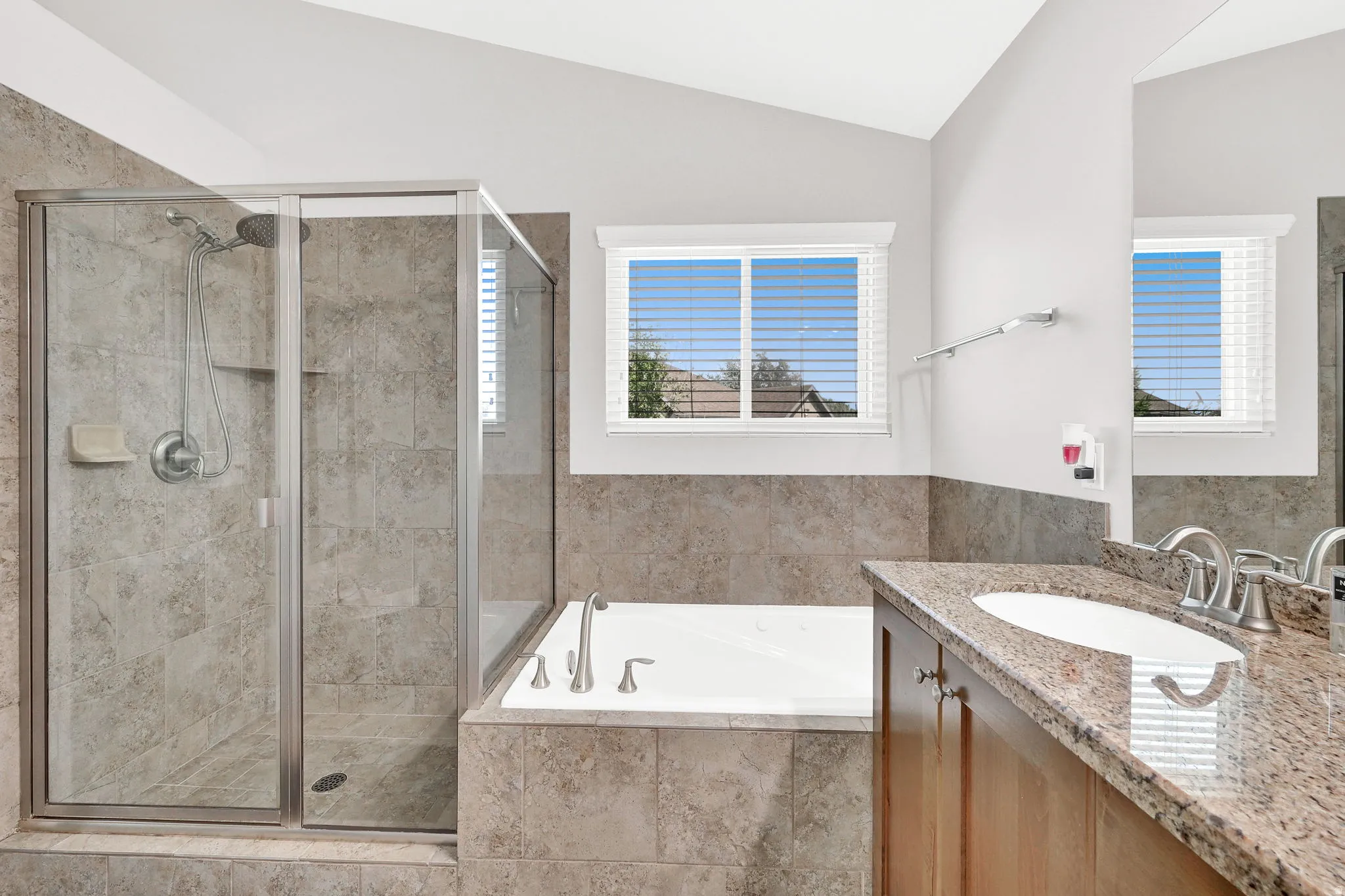 Glass-enclosed shower with tile surround, built-in soaking tub, wood-finish vanity, and stone countertop with an integrated sink