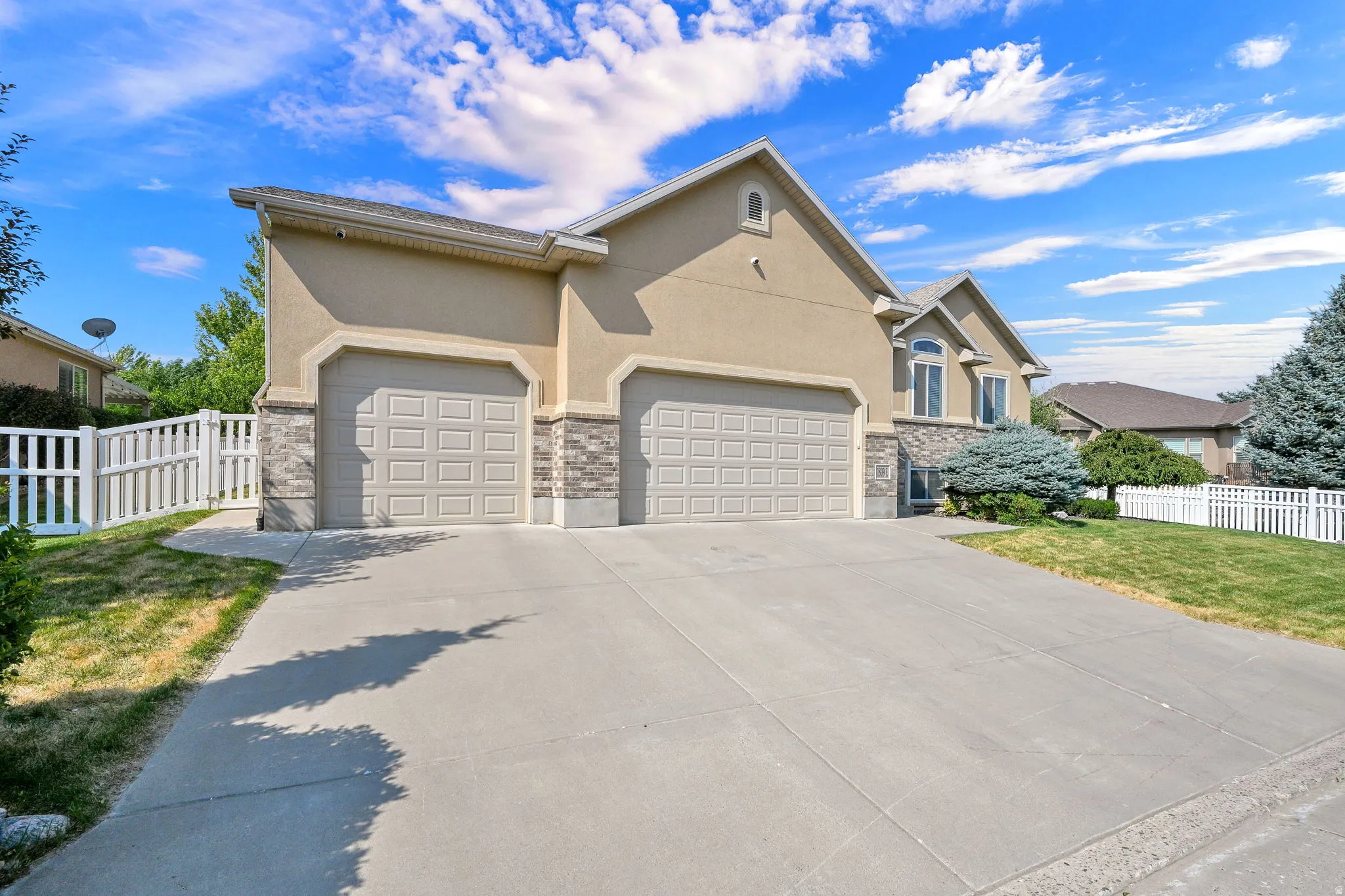 Stucco exterior with stone accents, two attached garages, concrete driveway, and white picket fencing
