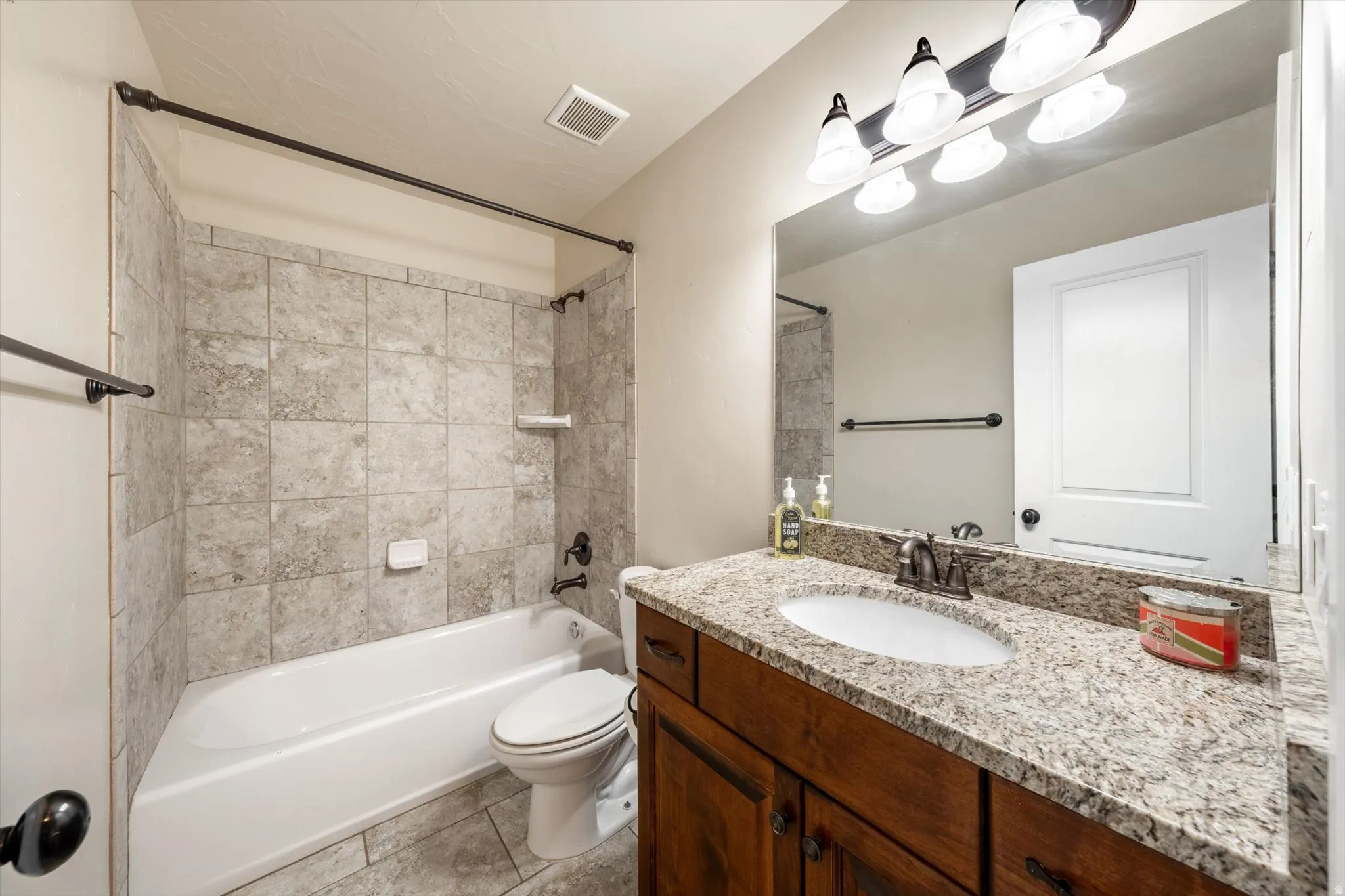 Bathroom featuring a shower-tub combination with tile surround, wood-finish vanity with a single sink, light-toned countertop, and tile flooring