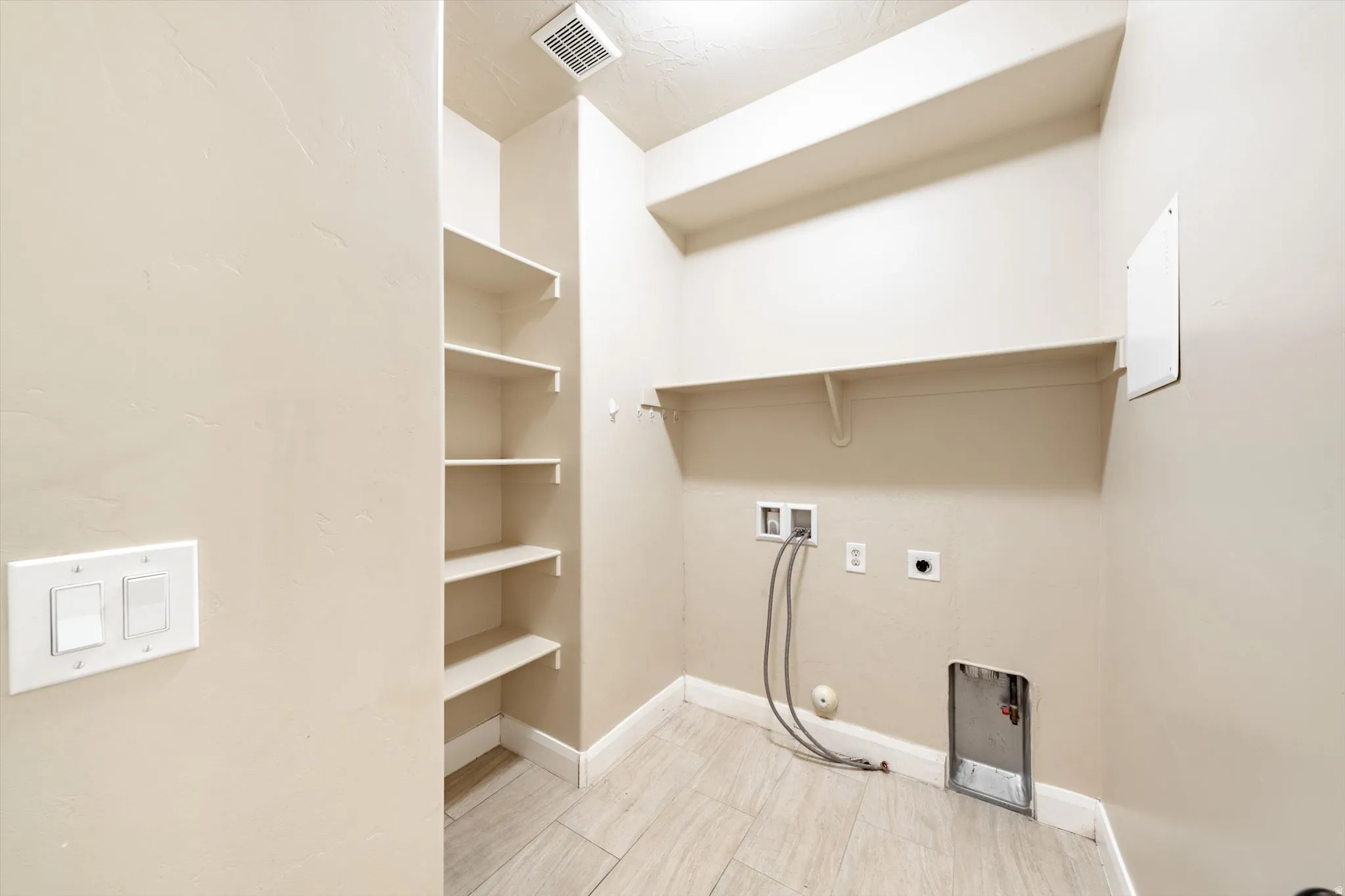 Utility room with tile flooring, built-in shelving, and a wall-mounted ventilation system