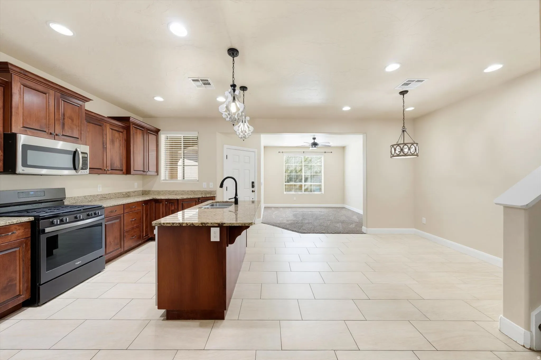 Kitchen features wood cabinetry, light-colored countertops, stainless steel microwave, gas range, and a kitchen island with sink