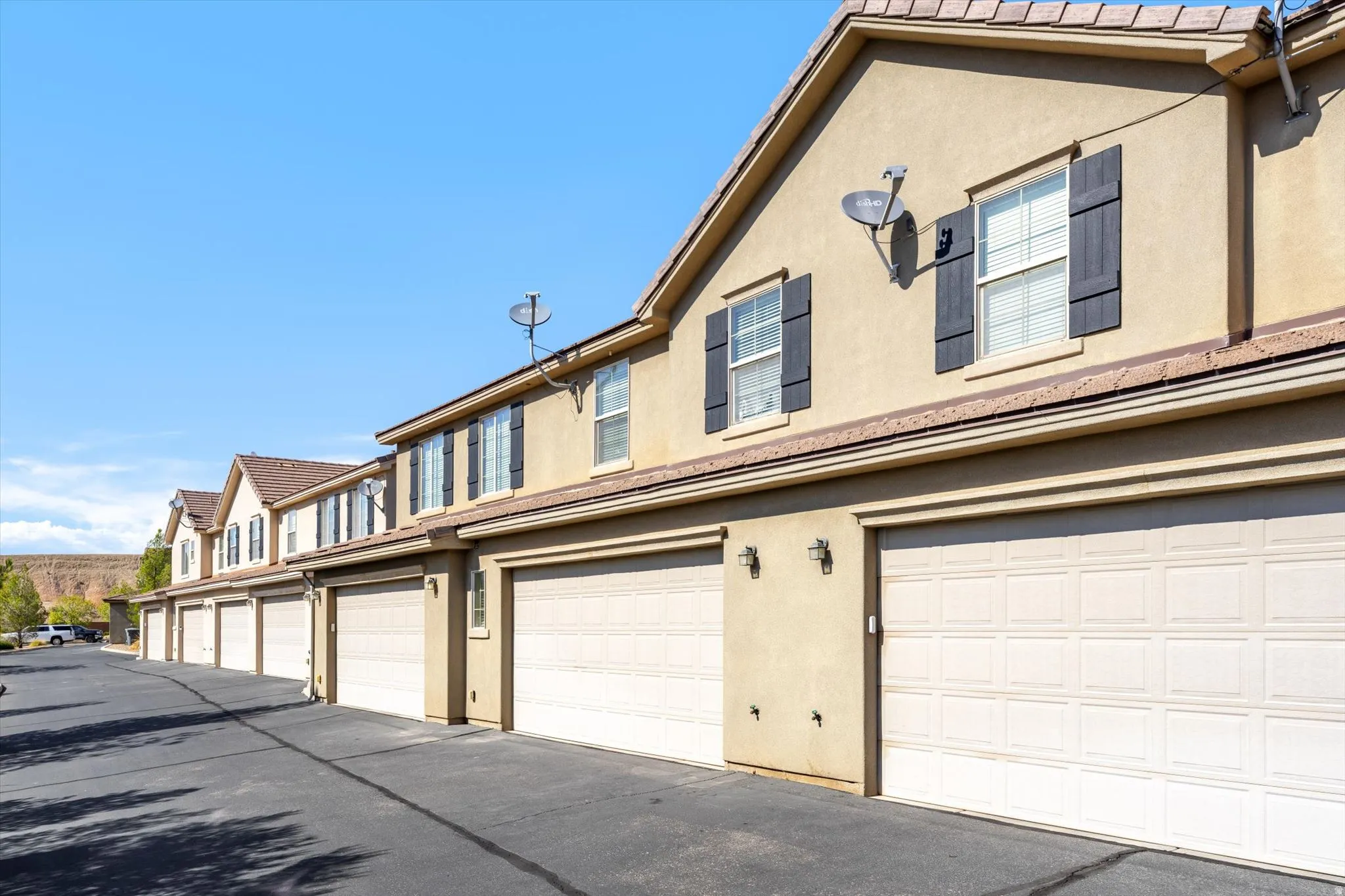 Stucco exterior with multiple garage entrances, upper-level windows with dark shutters, and a sloped roofline