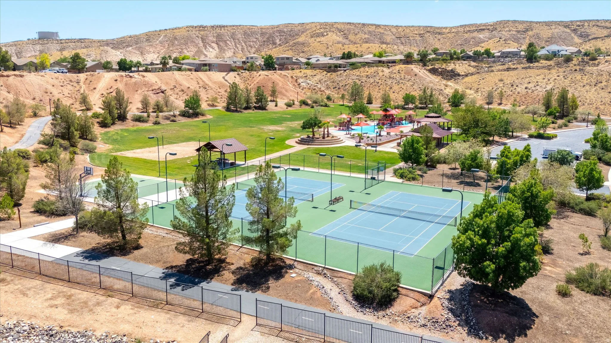 Expansive park setting featuring multiple tennis courts, a basketball court, a large grassy area, and a children's play area with water features