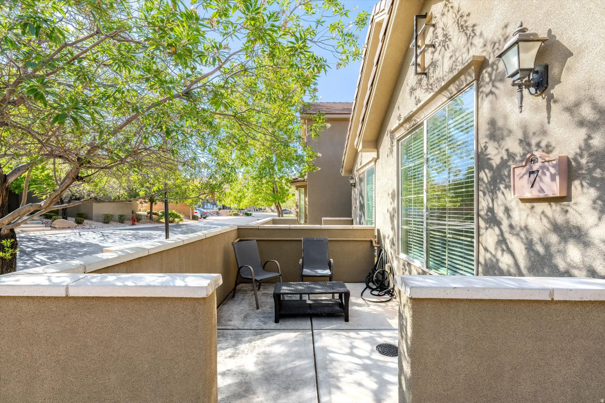 Private patio area with stucco walls, concrete flooring, and mature tree landscaping