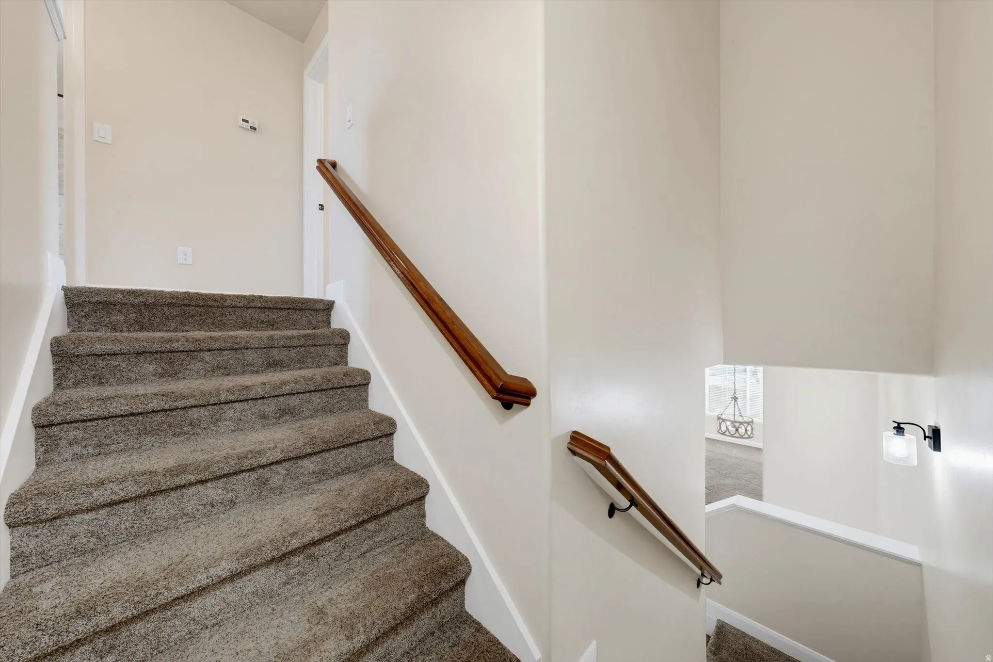 Carpeted staircase with a wood-finish handrail and integrated wall sconce