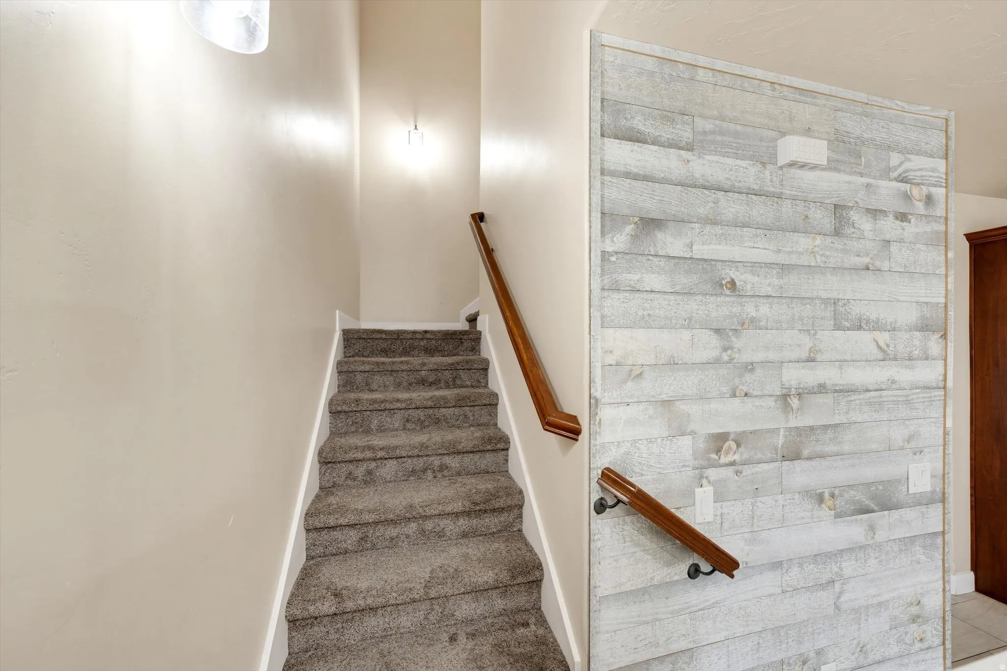 Carpeted staircase with wooden handrails and a shiplap accent wall