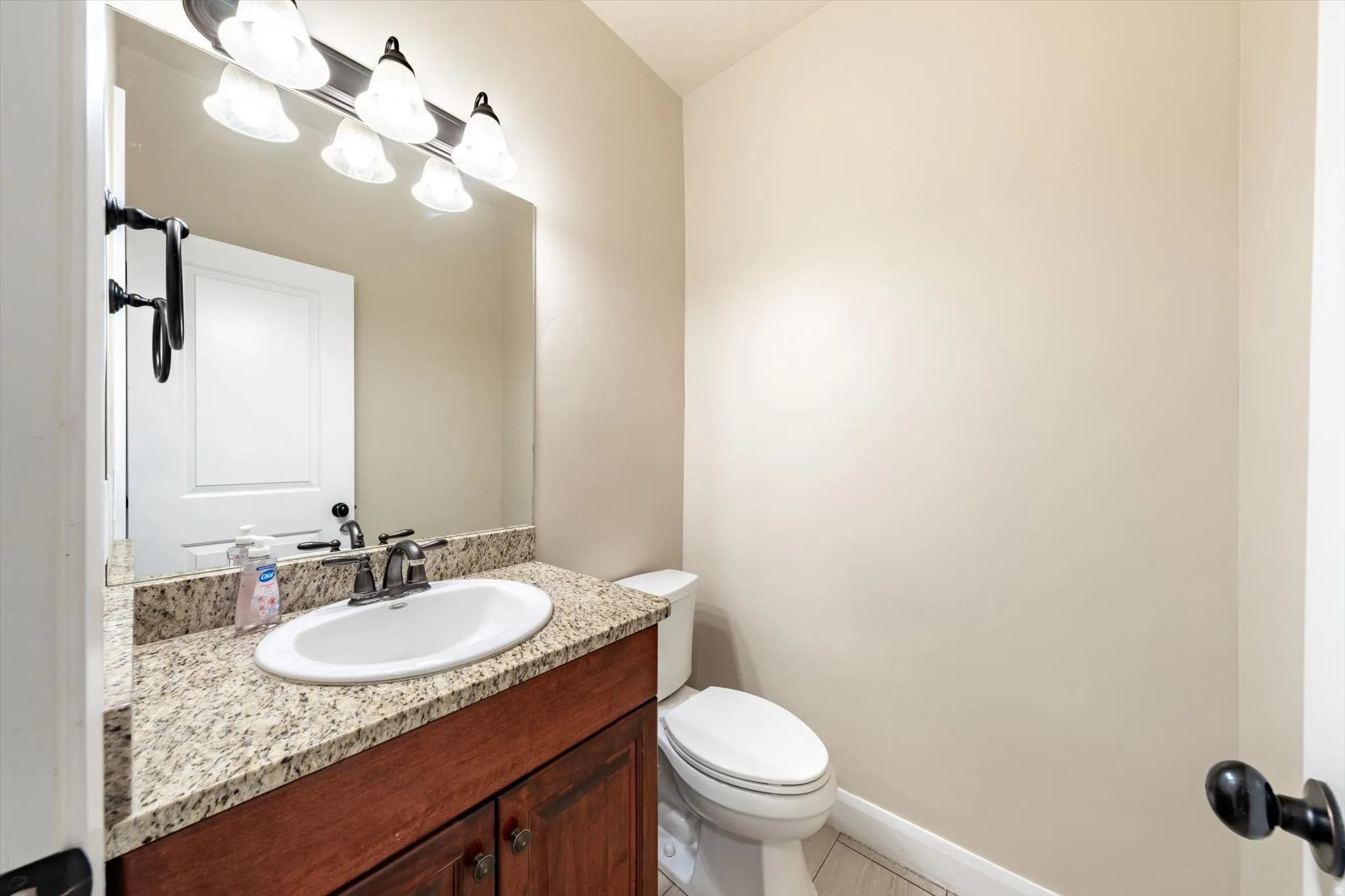 Vanity with a wood-finish base cabinet, stone countertop, undermount sink, and wall-mounted lighting fixture