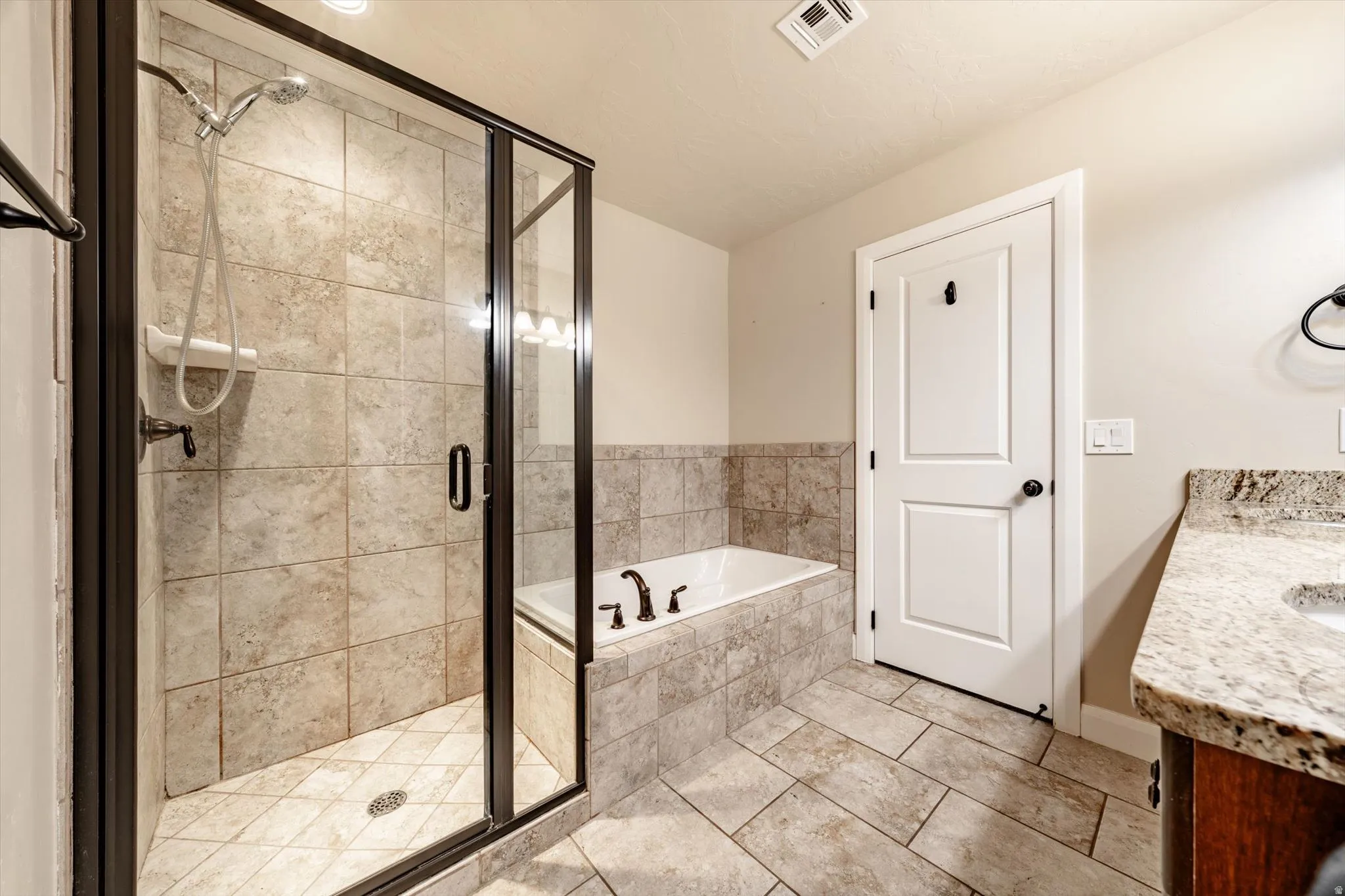 Tiled shower with a clear glass enclosure, a built-in tub with matching tile surround, and a vanity featuring a stone countertop