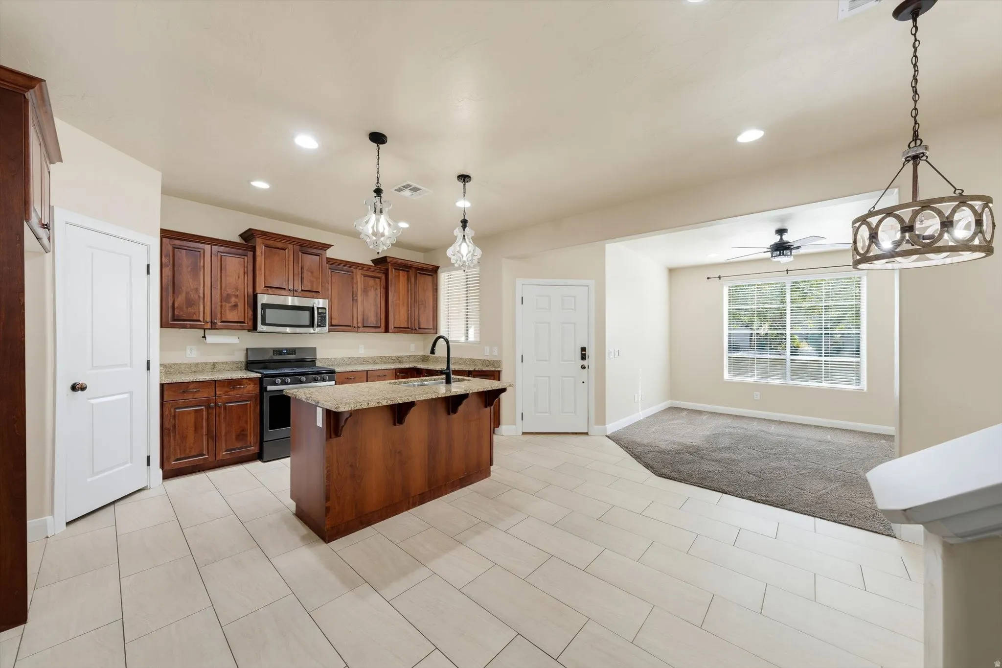 Kitchen featuring wood cabinetry, granite countertops, stainless steel appliances, and a central island with sink