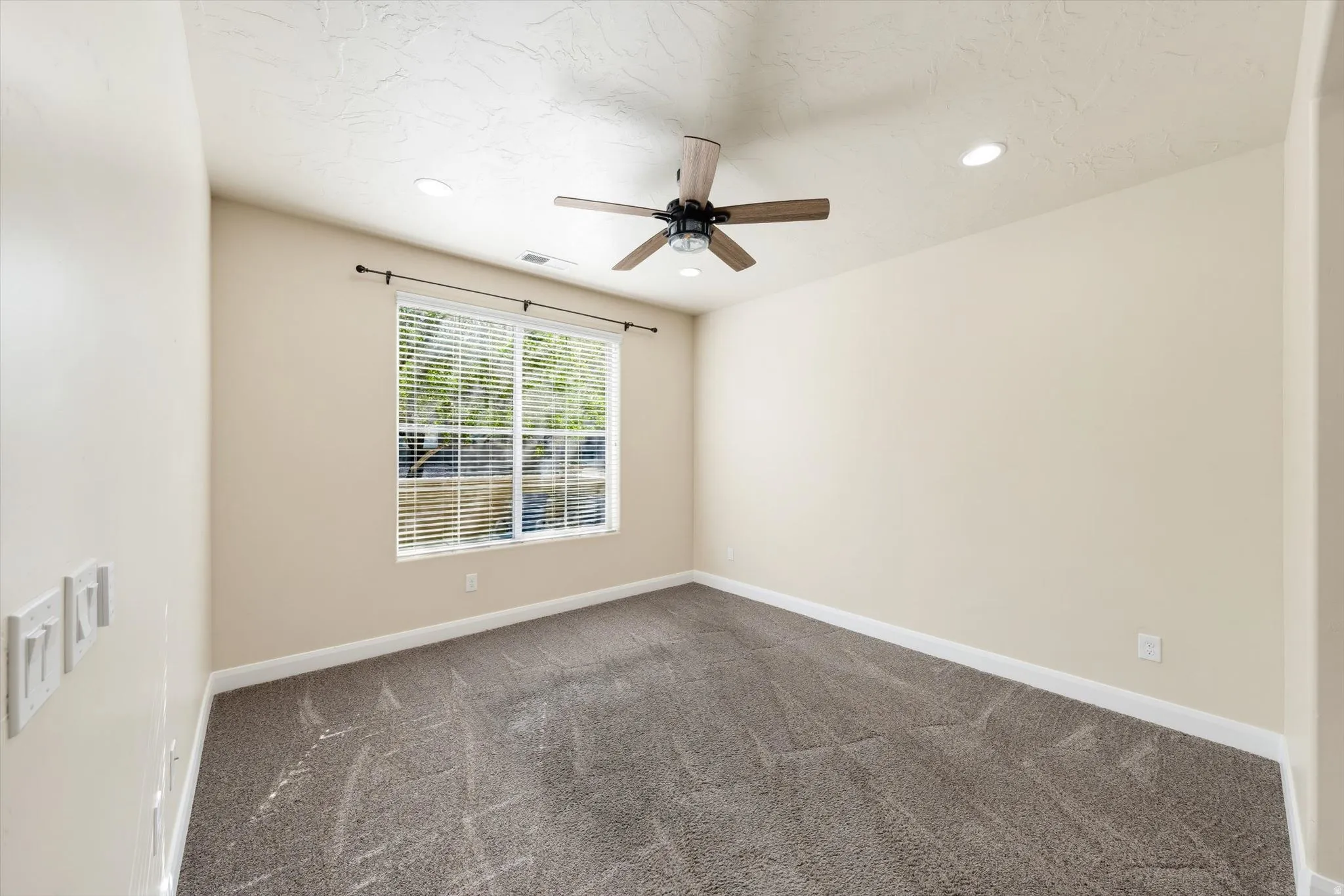 Spacious room featuring neutral carpeting, a window with blinds, and a ceiling fan with integrated lighting