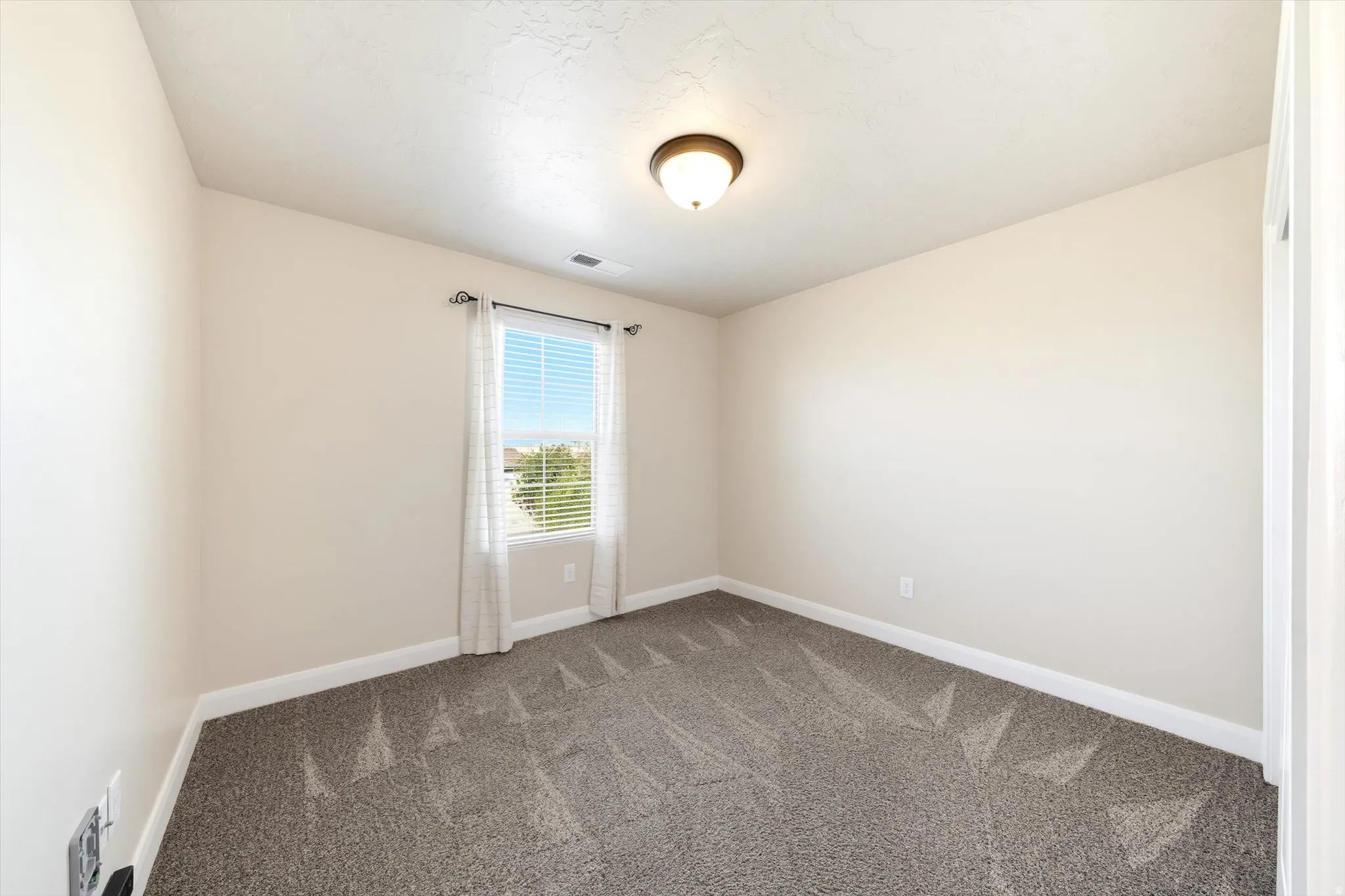 Neutral-toned walls, textured carpeting, window with blinds, and a ceiling-mounted light fixture