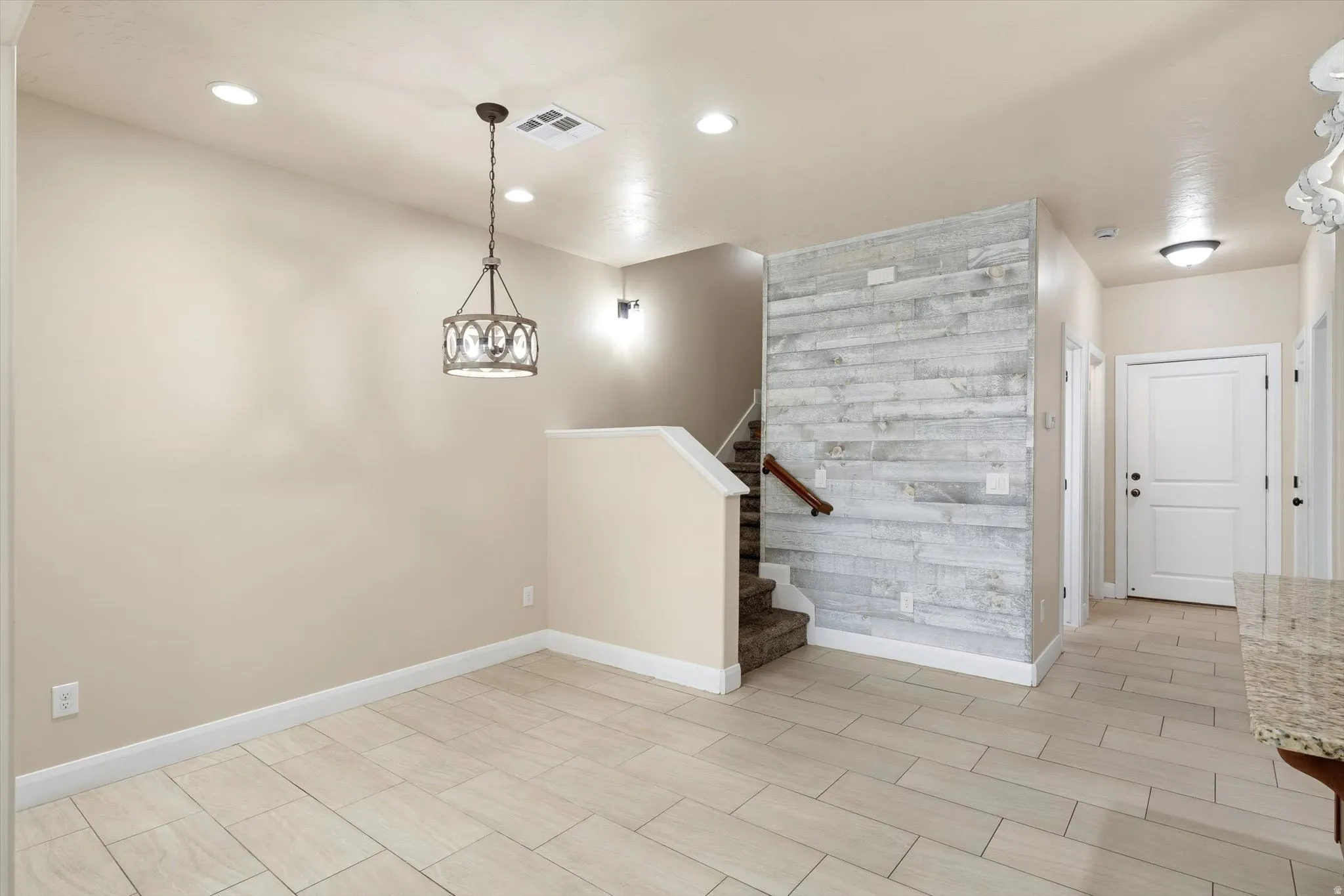 Recessed lighting and a decorative chandelier illuminate the space, featuring wood-look tile flooring
