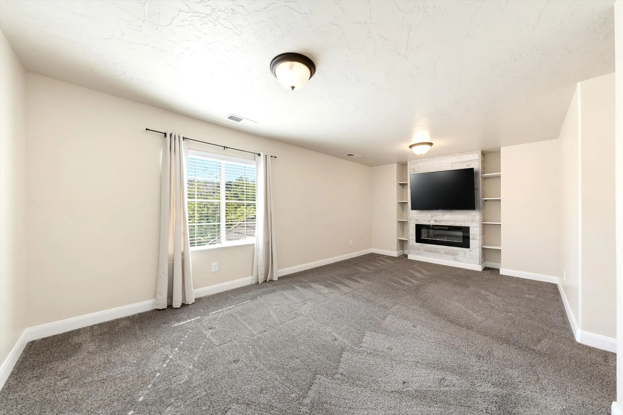 Spacious recreation room featuring neutral carpeting, recessed ceiling lighting, and a built-in entertainment center with fireplace and shelving