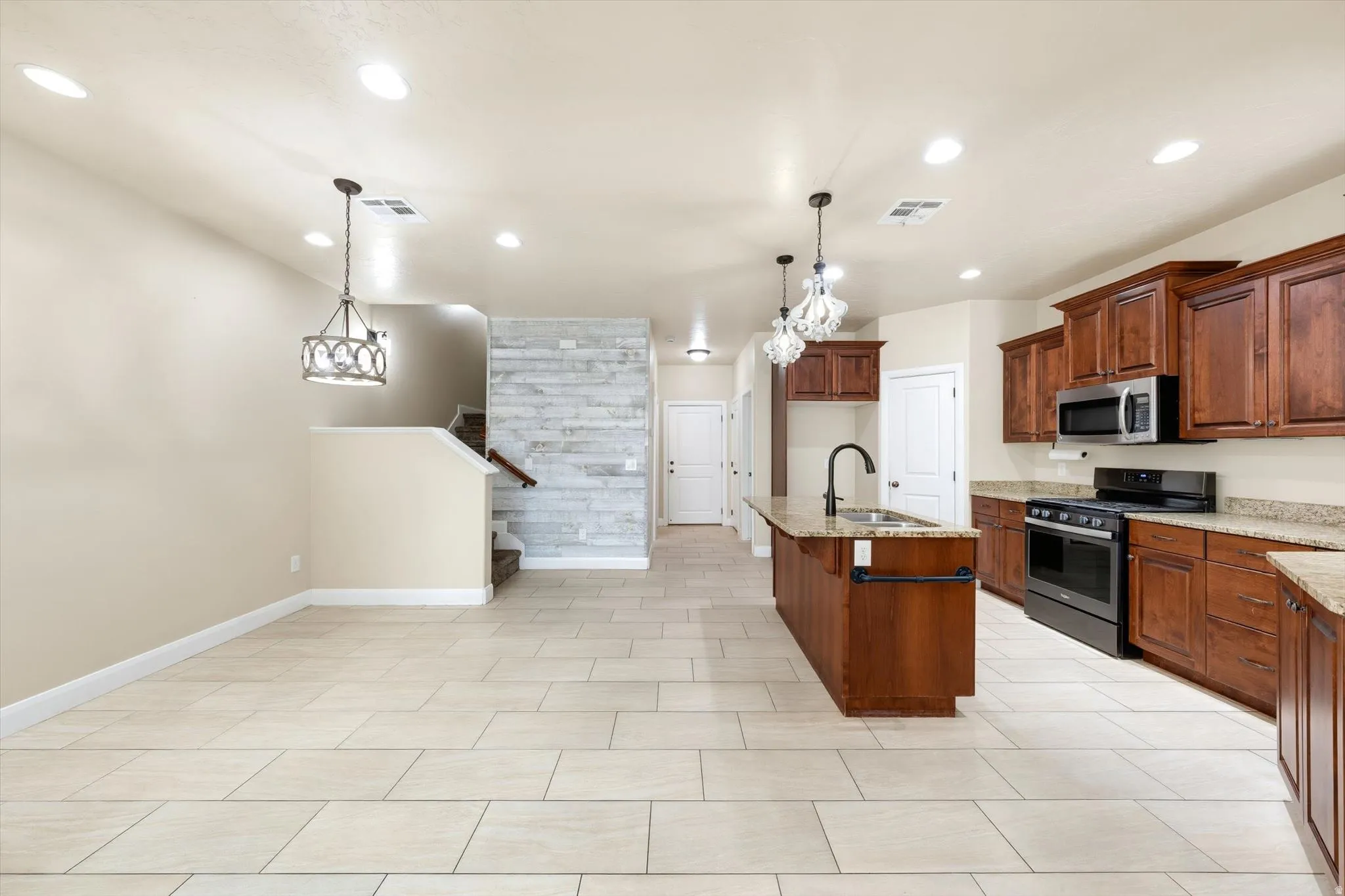 Kitchen and living area featuring tile flooring, wooden cabinetry, stainless steel appliances, and recessed lighting