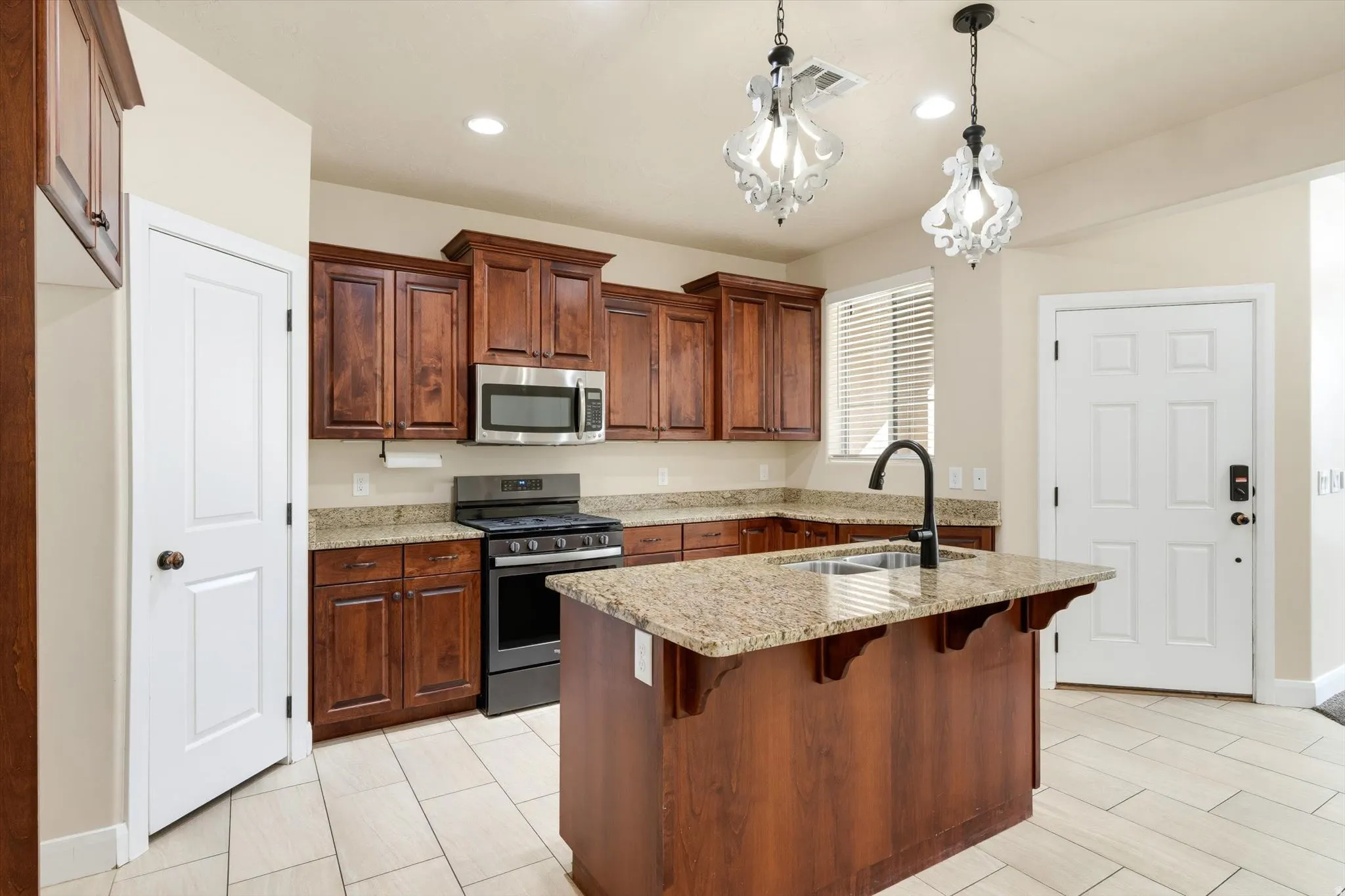 Dark wood-finish cabinetry with stainless steel appliances, granite countertops, kitchen island with sink, and tile flooring
