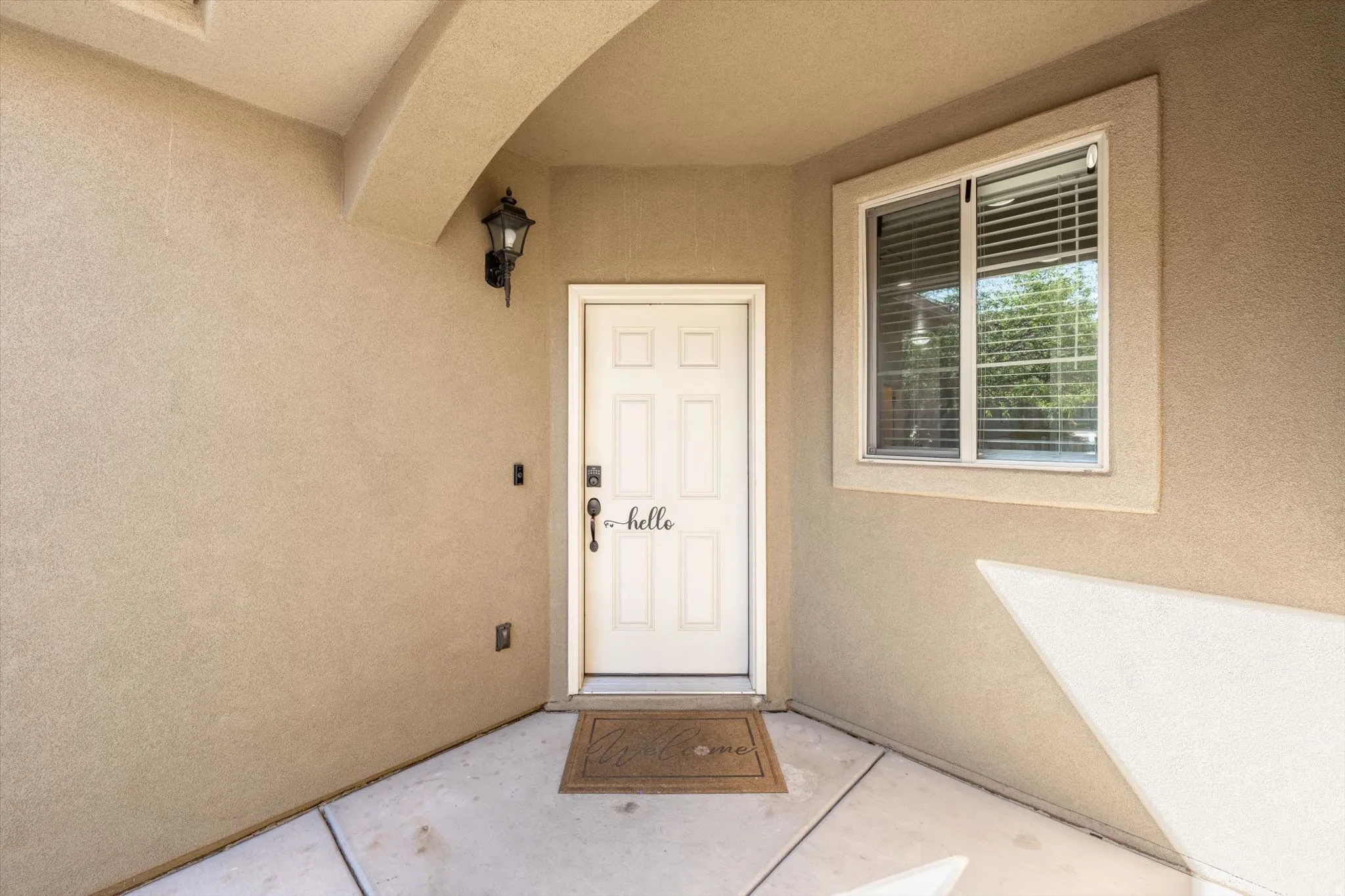 Arched entryway featuring a paneled entry door, exterior sconce lighting, and an adjacent window with horizontal blinds
