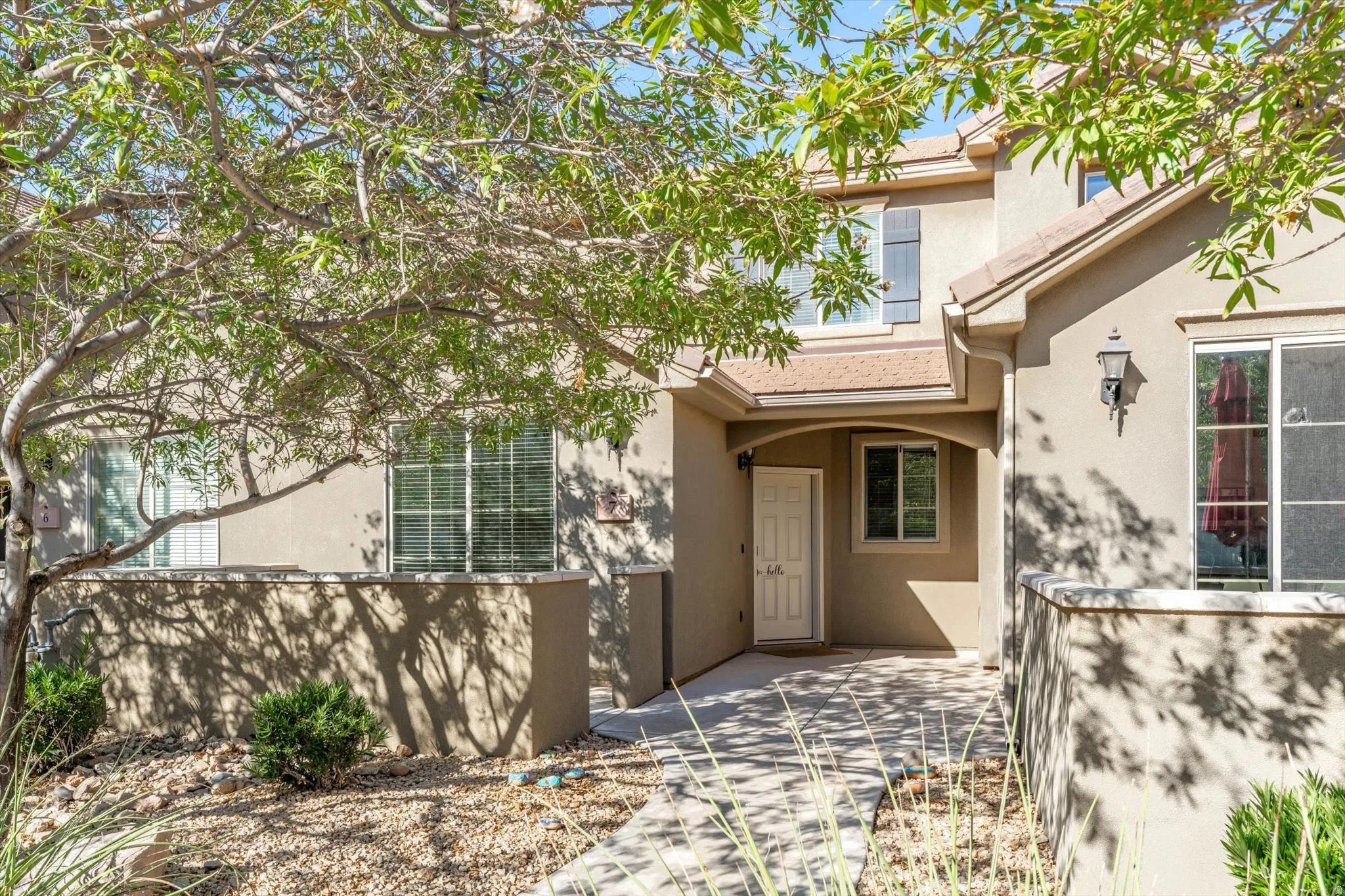 Stucco exterior with a tiled entry archway, white paneled entry door, and exterior sconce lighting