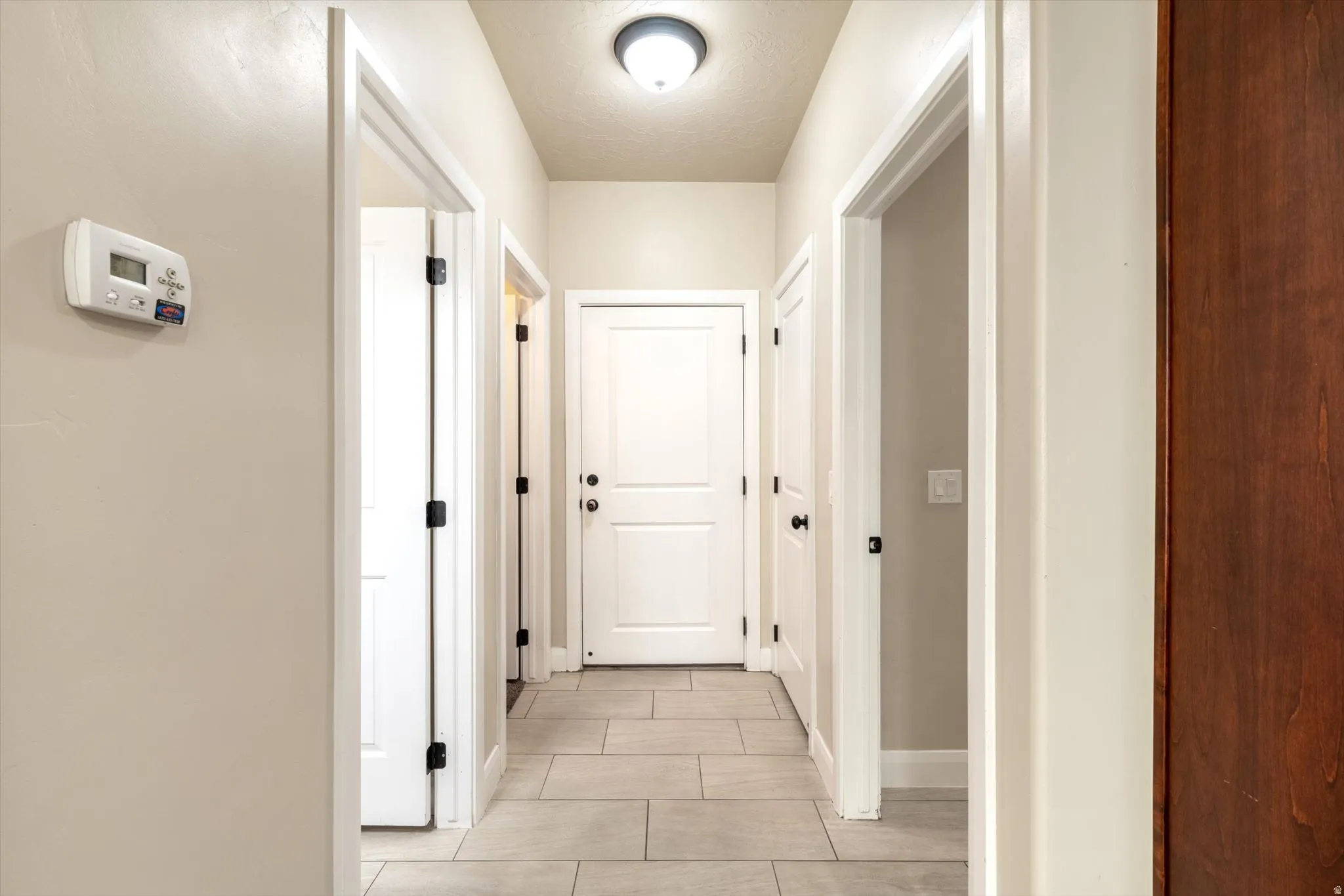 Hallway featuring light-toned wall paint, tiled flooring, white doors with dark hardware, and a ceiling-mounted light fixture